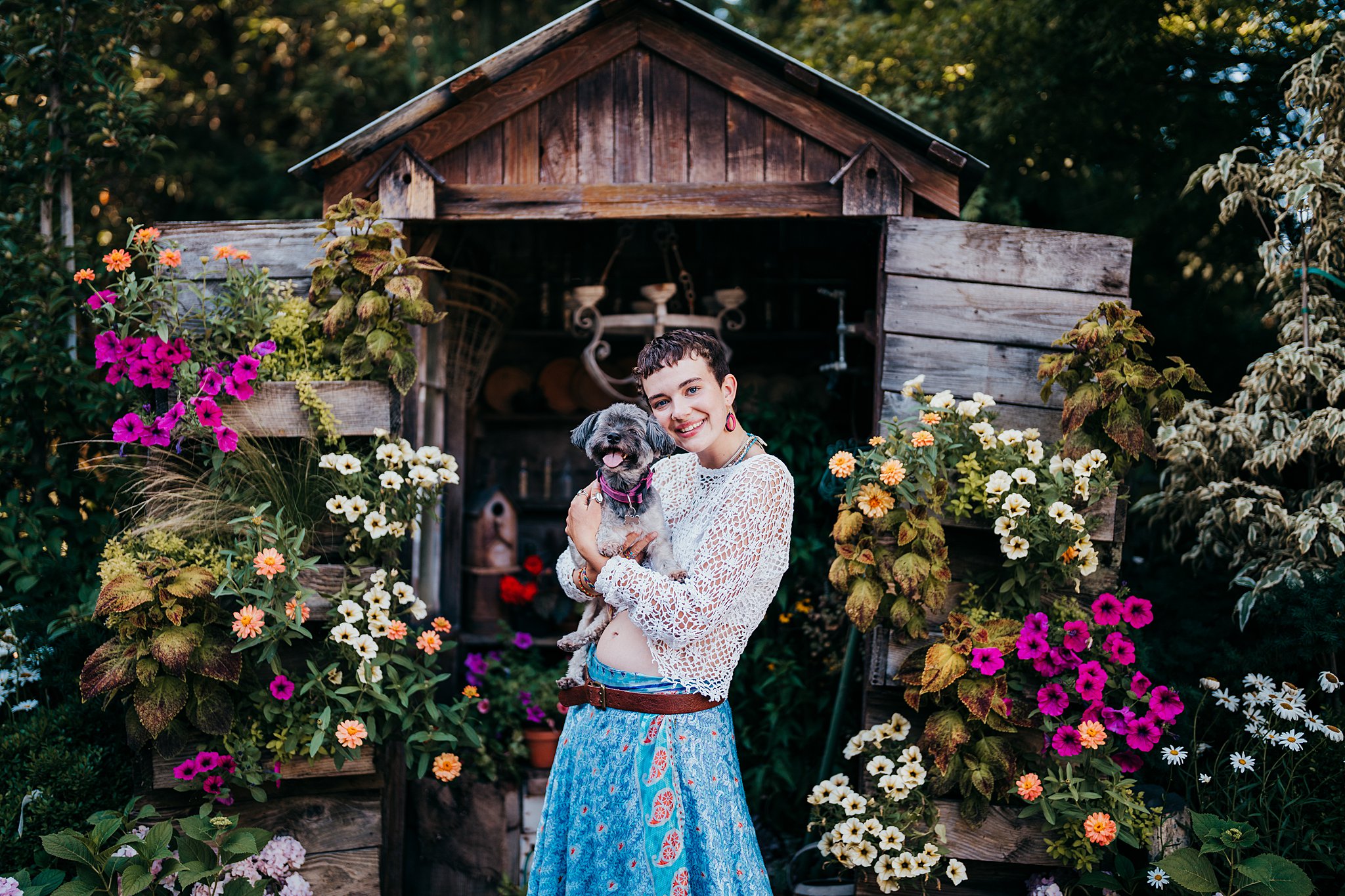 A woman in a blue dress and white top stands in front of a garden shed holding a small puppy Seattle Photoshoot Locations