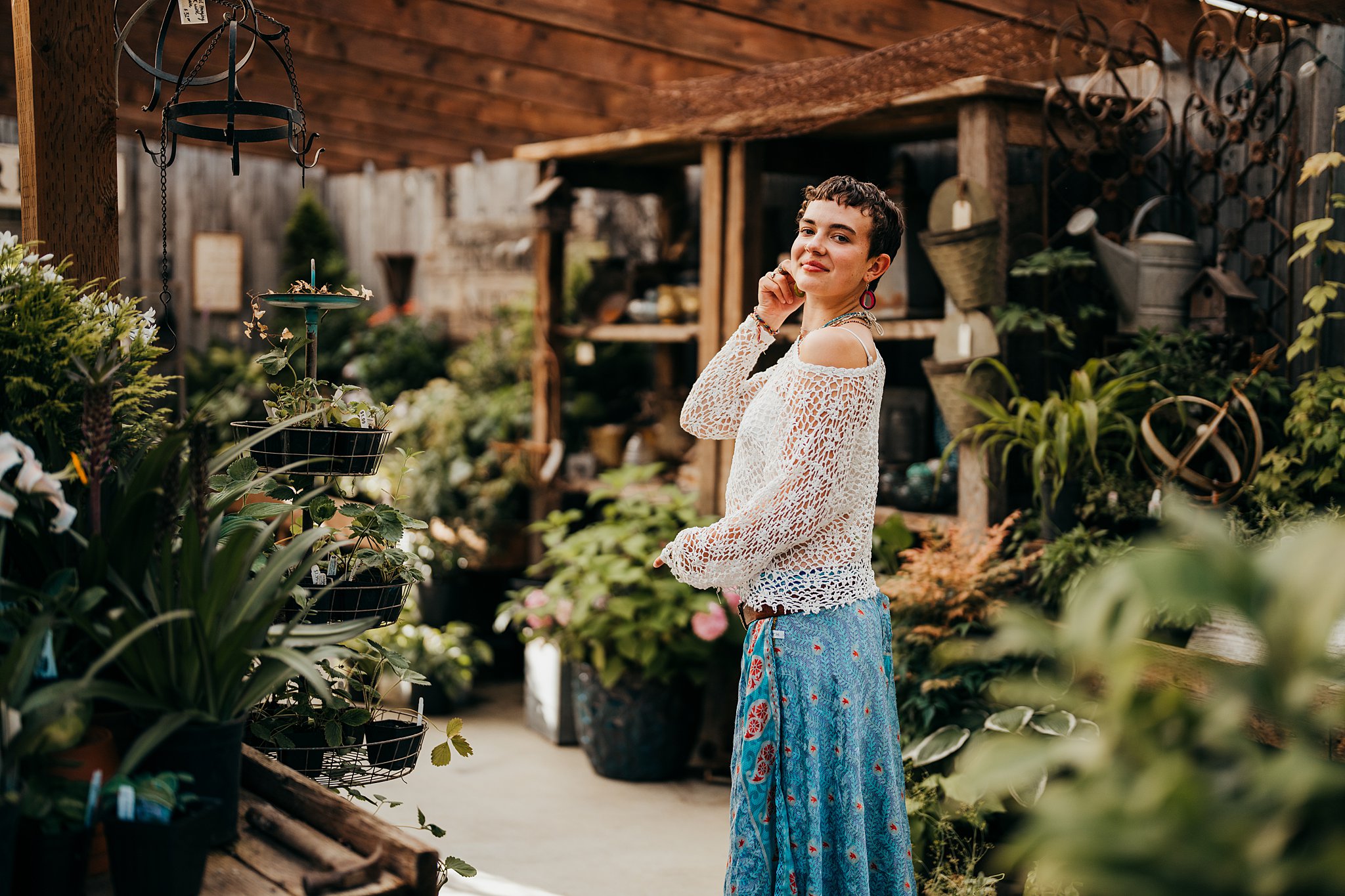 A woman in a blue skirt stands inside a garden shed with a hand on her cheek