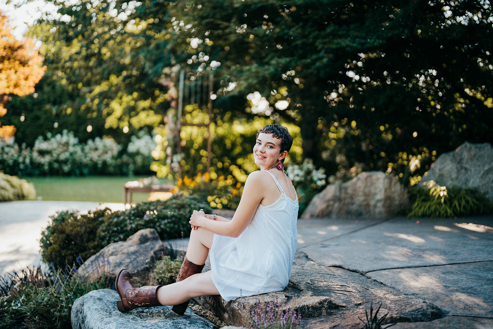 A woman in a white dress and brown booth sits on some rocks in a garden Seattle Photoshoot Locations