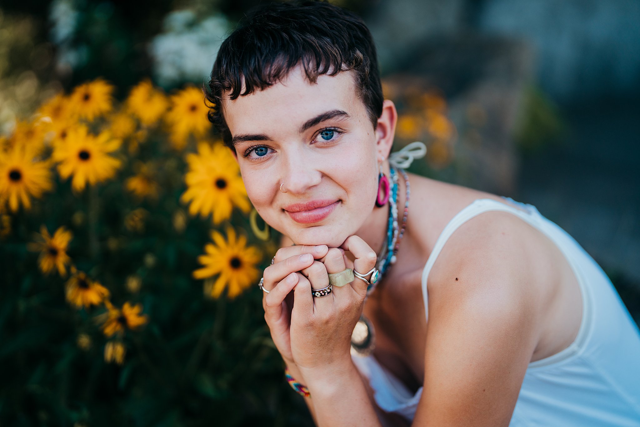 A woman wearing multiple rings and a white top sits with some yellow daisies Seattle Photoshoot Locations