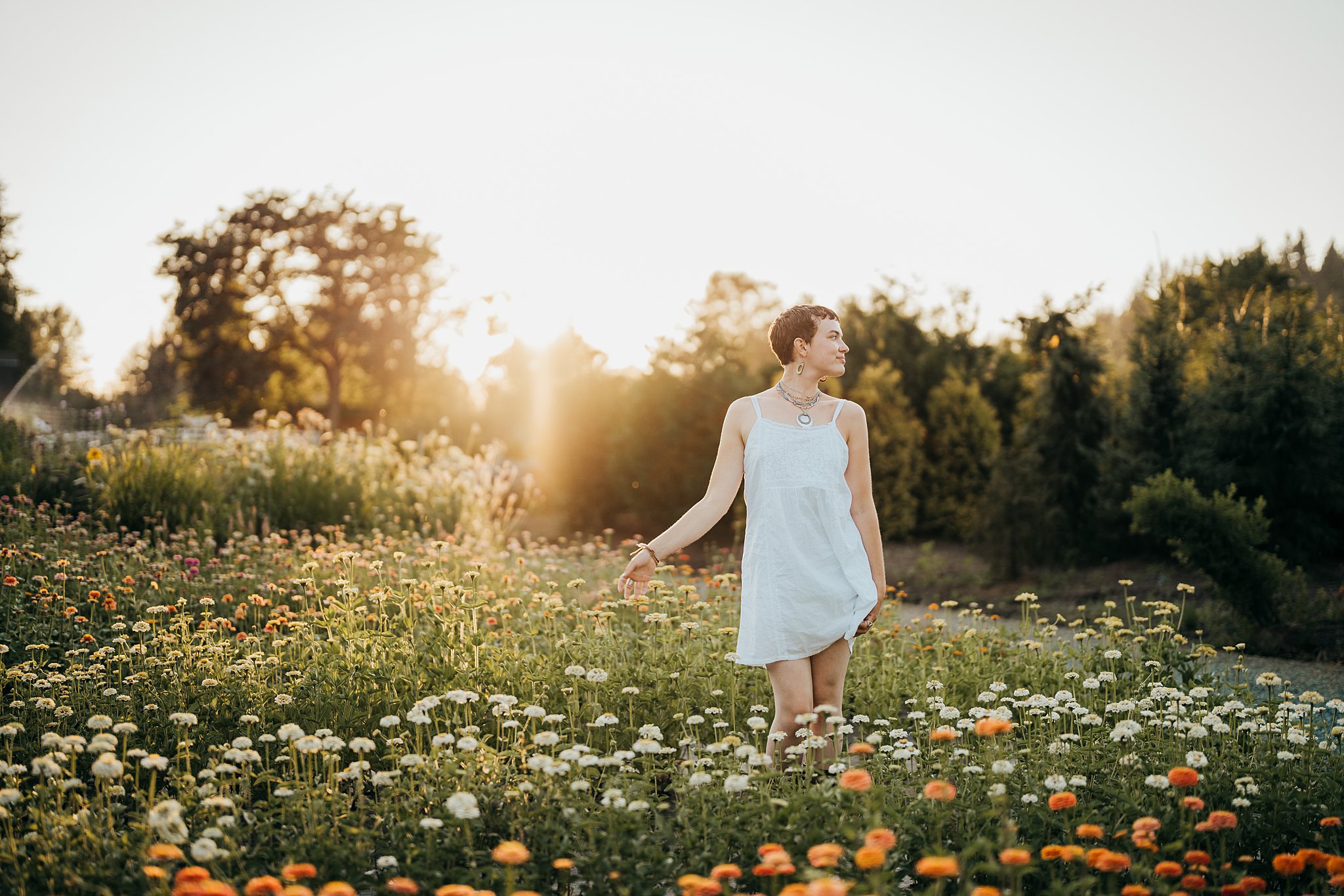 A woman in a white dress stands in a field of colorful daisies at sunset Seattle Photoshoot Locations