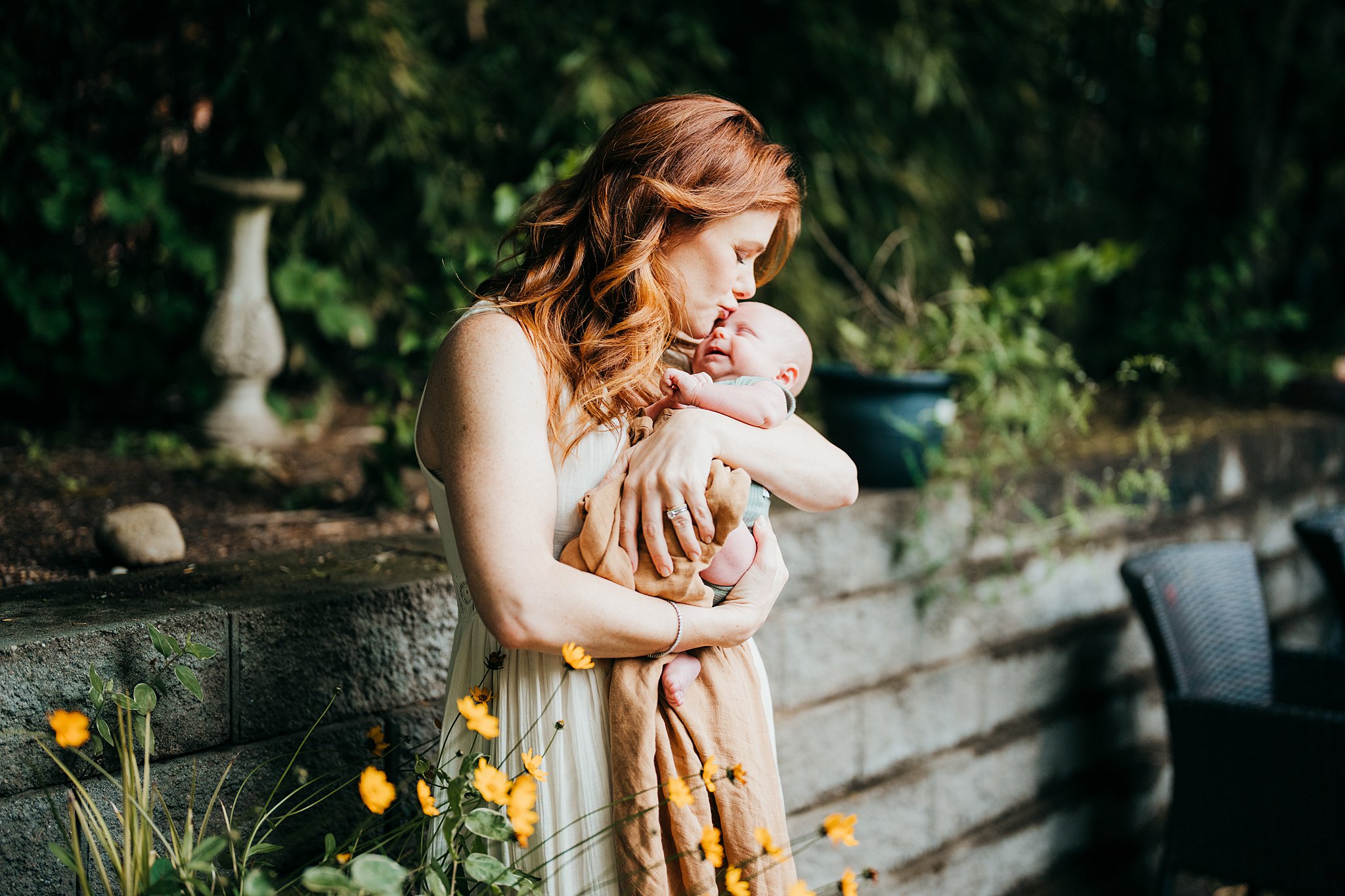 A mother in a white dress kisses her smiling newborn baby in her arms Seattle doulas