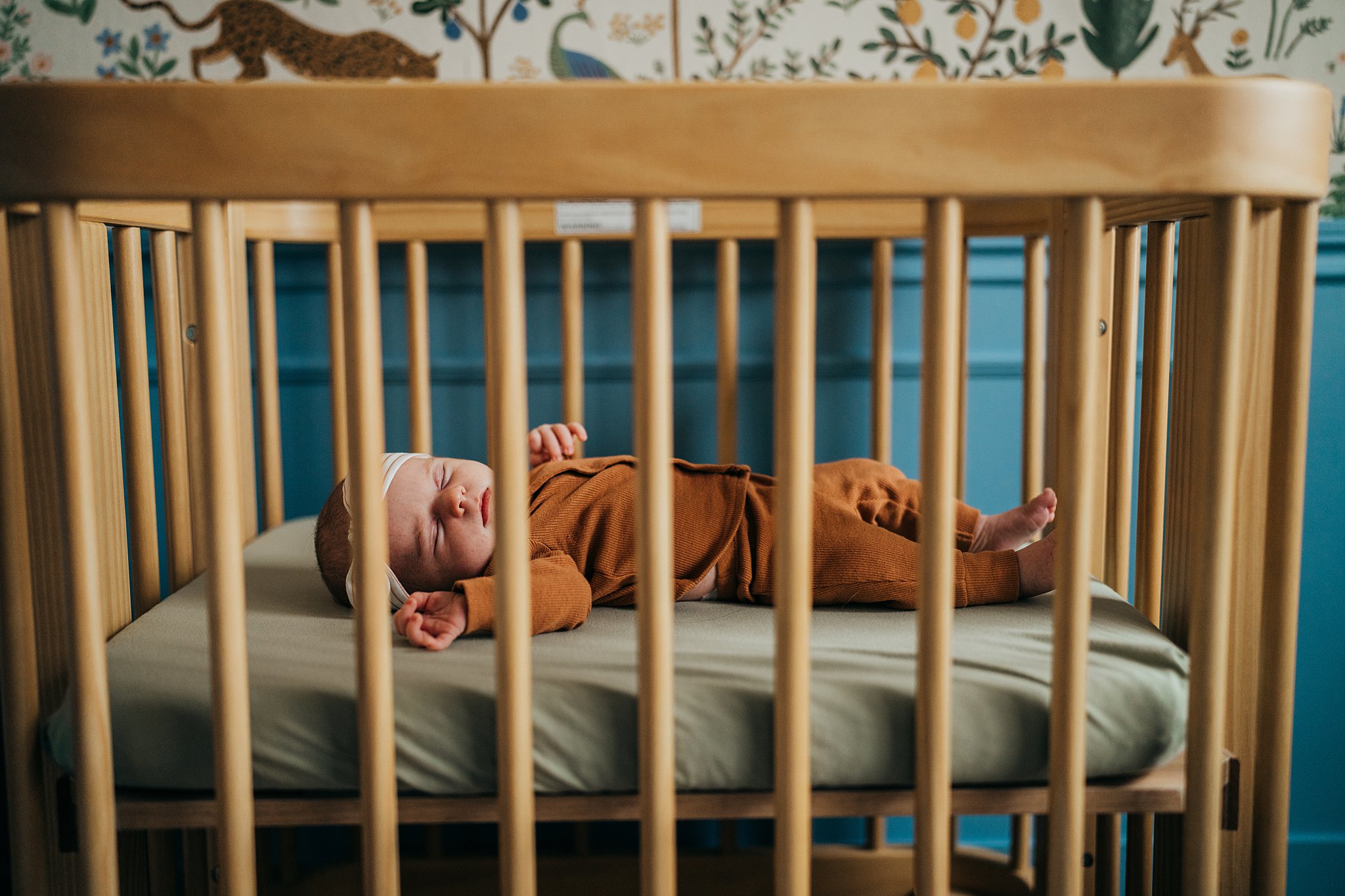 A newborn baby in a brown onesie sleeps in a wooden crib center for women's health at evergreen
