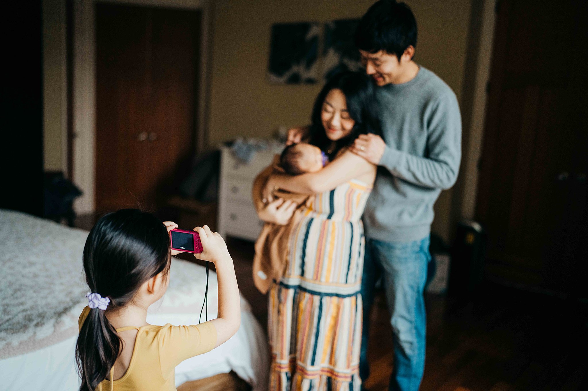 A young girl takes a picture of her parents holding their newborn baby in mom's arms with a pink camera seattle midwives