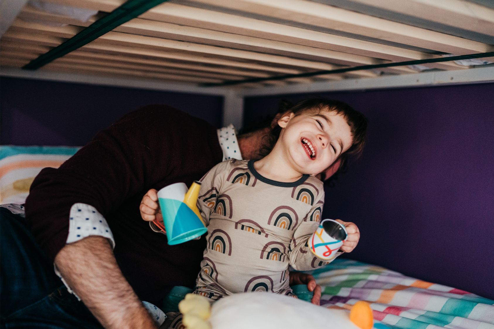a toddler girl playing and laughing with dad on her bed