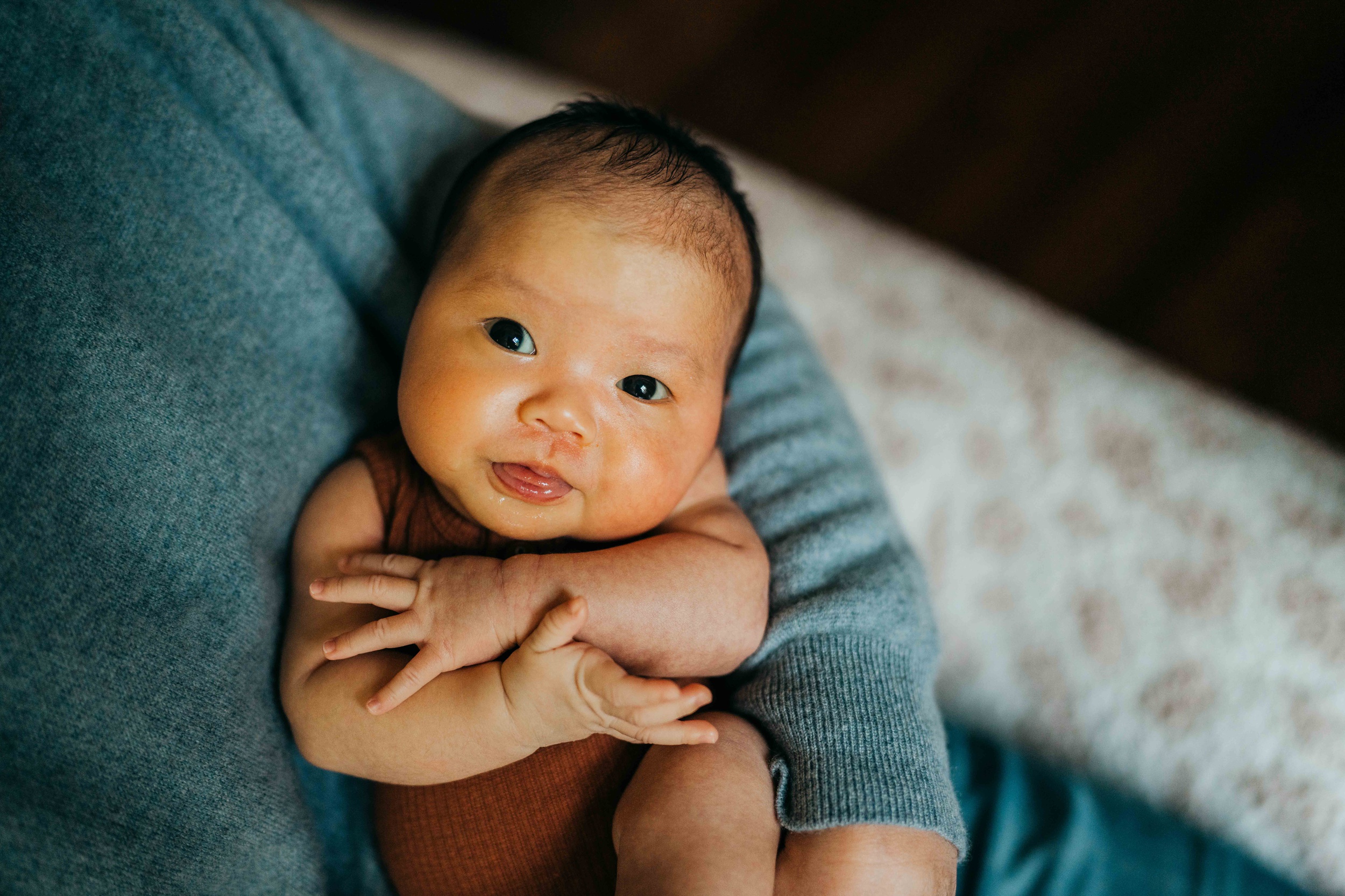 A newborn baby smiles while looking up at mom while laying in her arms after a 3d ultrasound in seattle