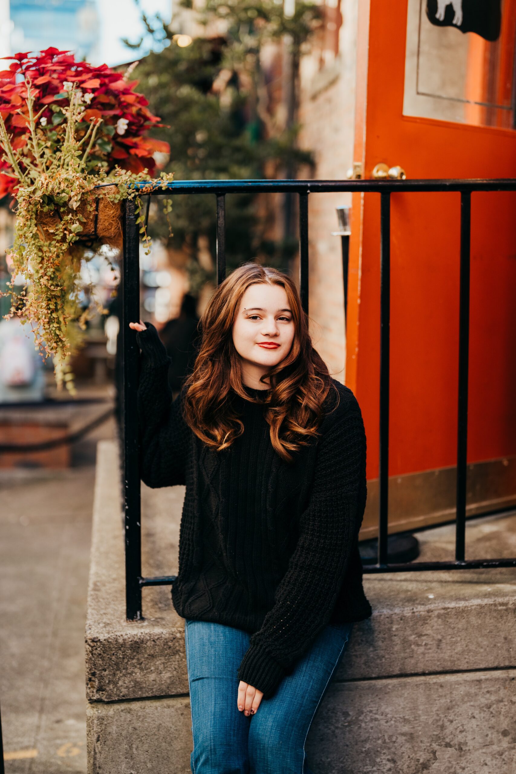 A Ballard High School senior in a black sweater sits on storefront steps leaning on the railing smiling