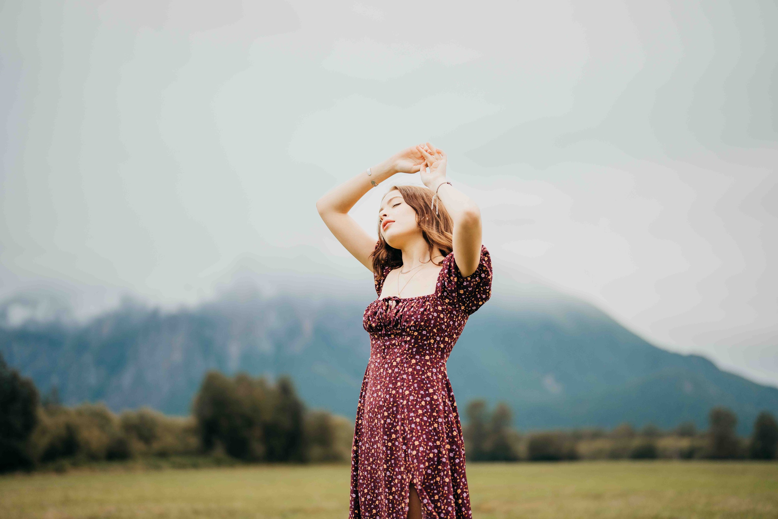 A teenage girl in a purple dress dances in a meadow near the mountains