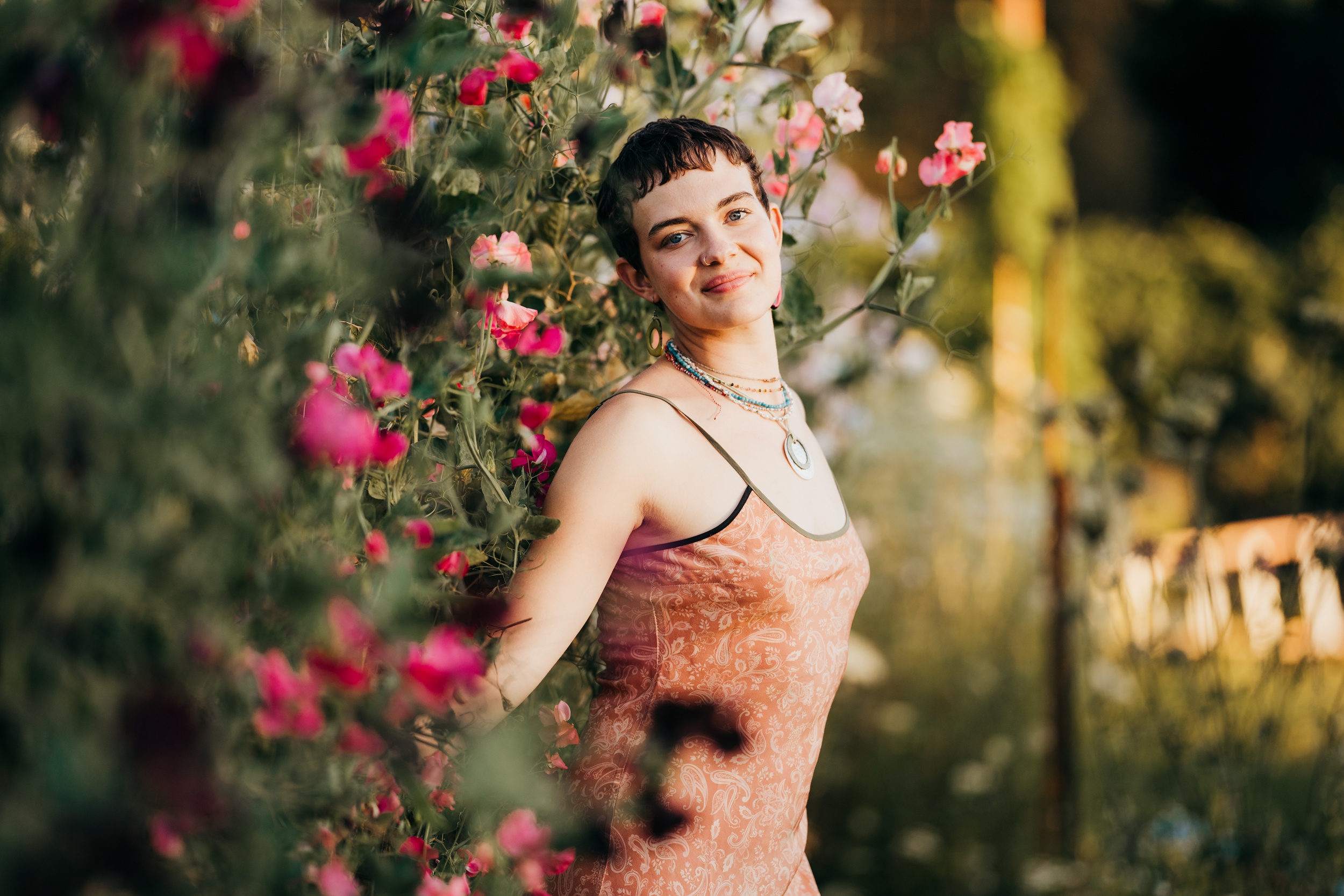 A Mercer Island High School senior in a paisley dress leans in a wall of pink flowers