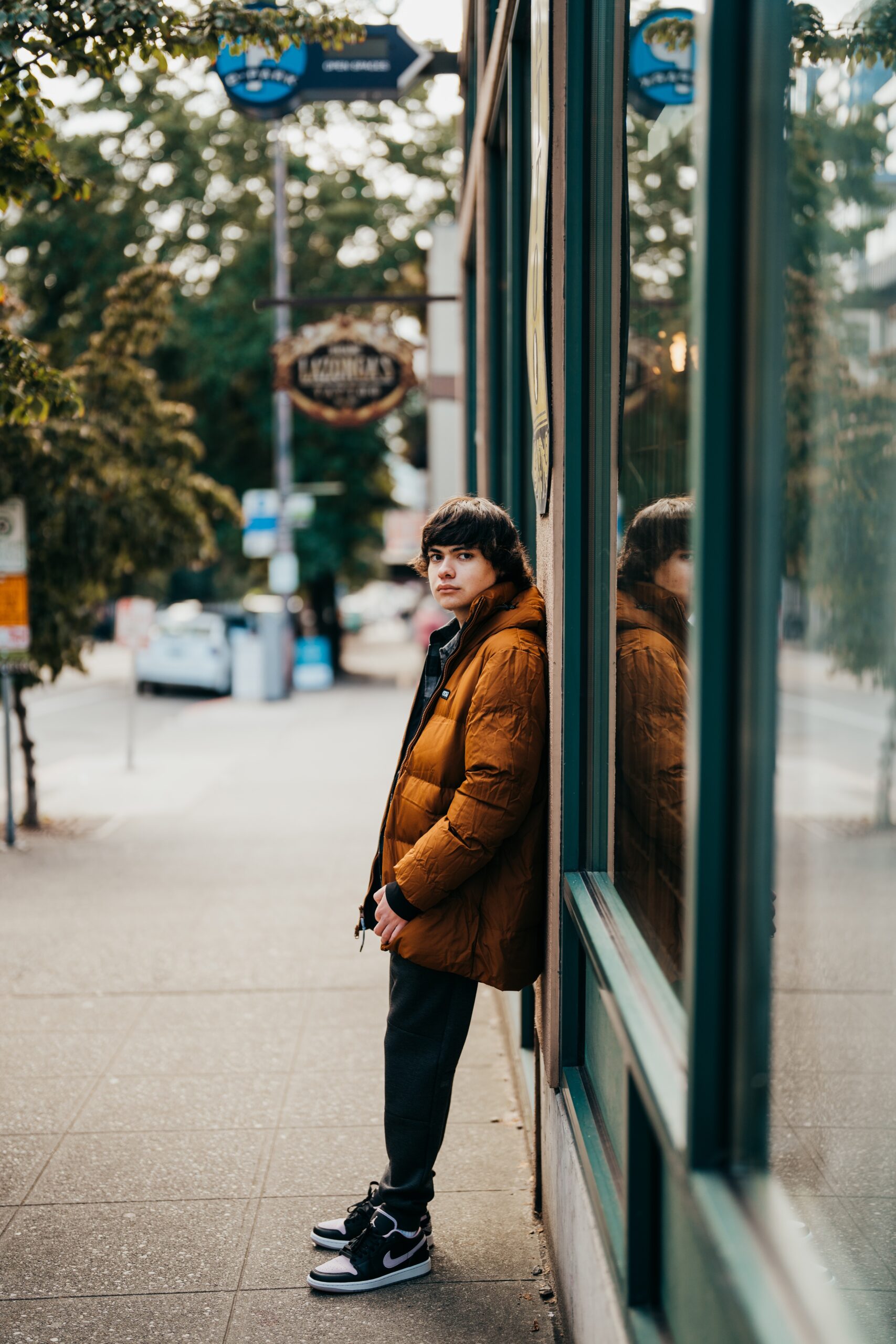 A Mercer Island High School senior in a brown jacket leans on a storefront entrance