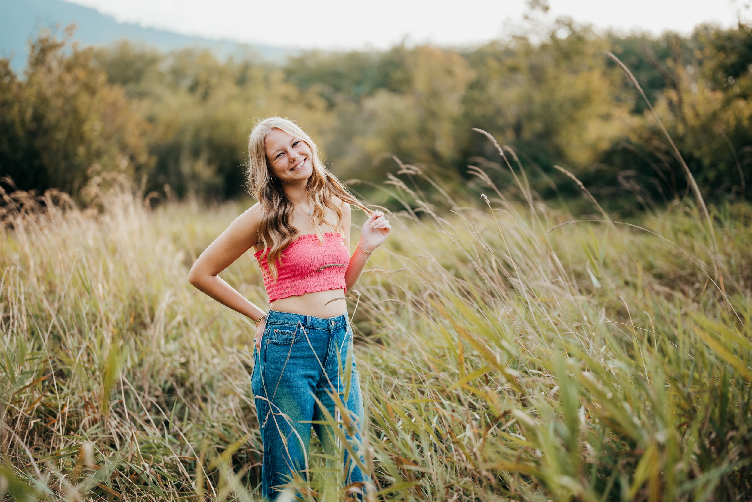 A Roosevelt High School senior in a pink top and jeans twirls her hair in a field of tall grass