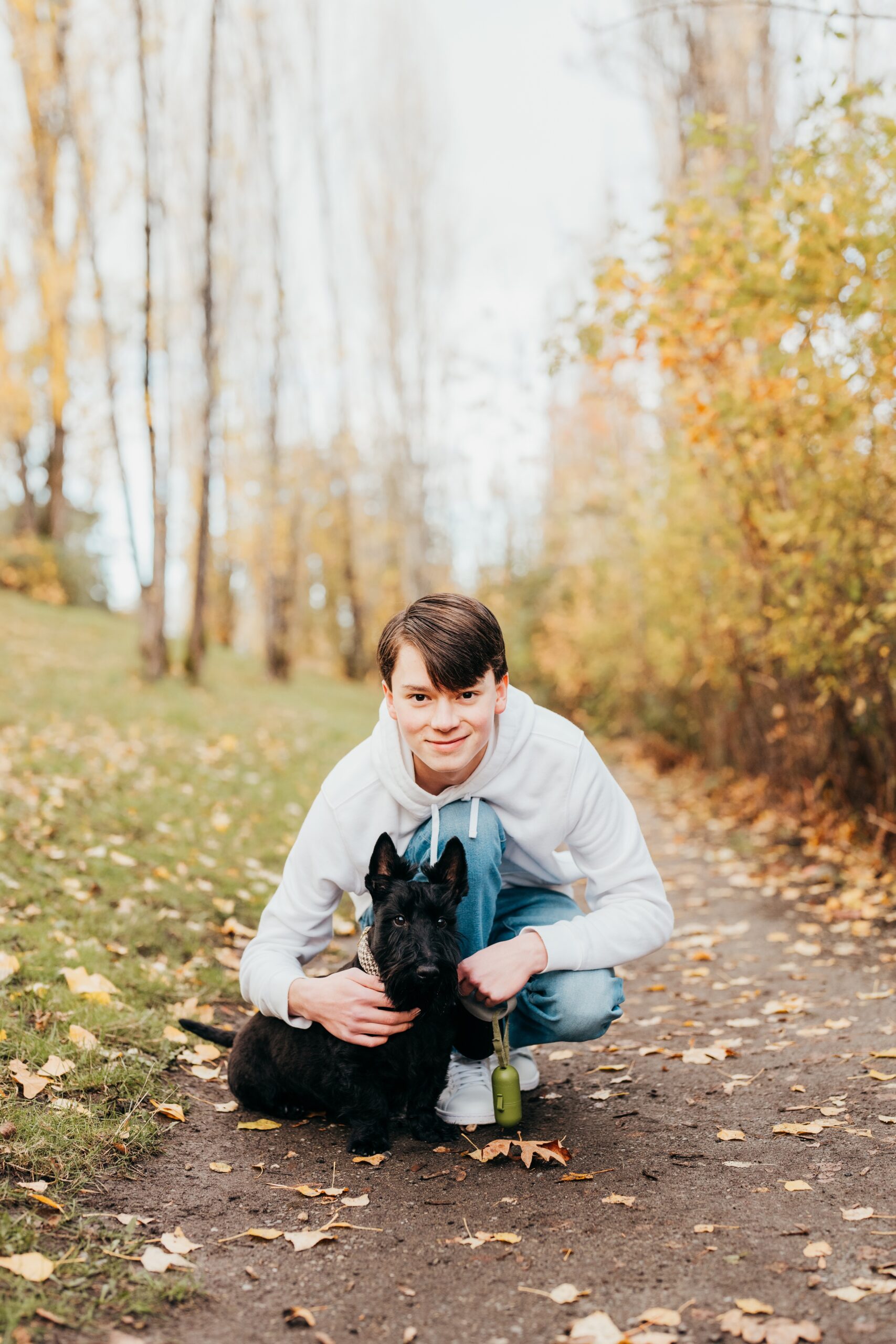 A happy teenage boy hugs his small black dog in a park trail in a white hoodie after some act prep in seattle