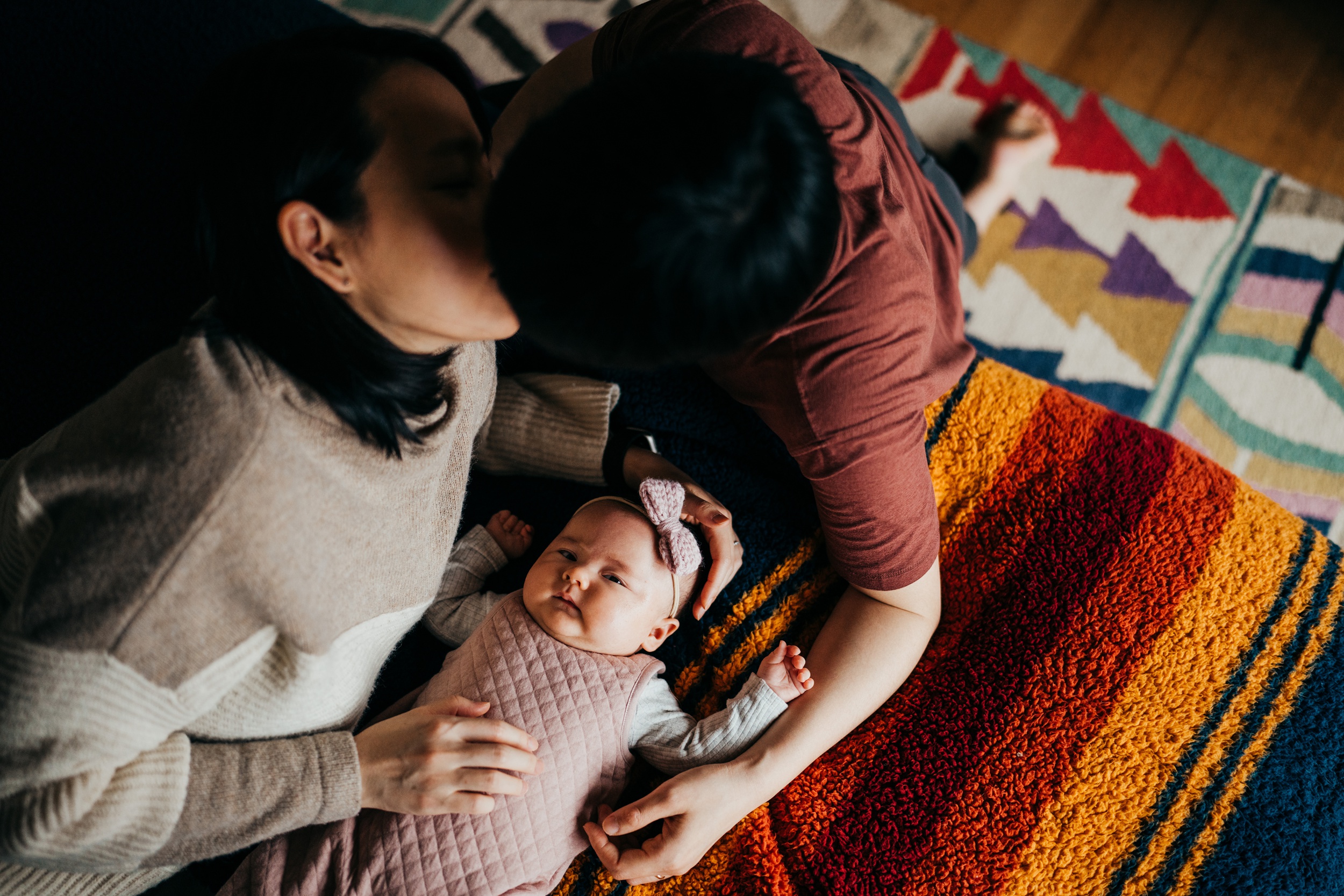 Happy new parents kiss while snuggling on a bed over their newborn baby girl