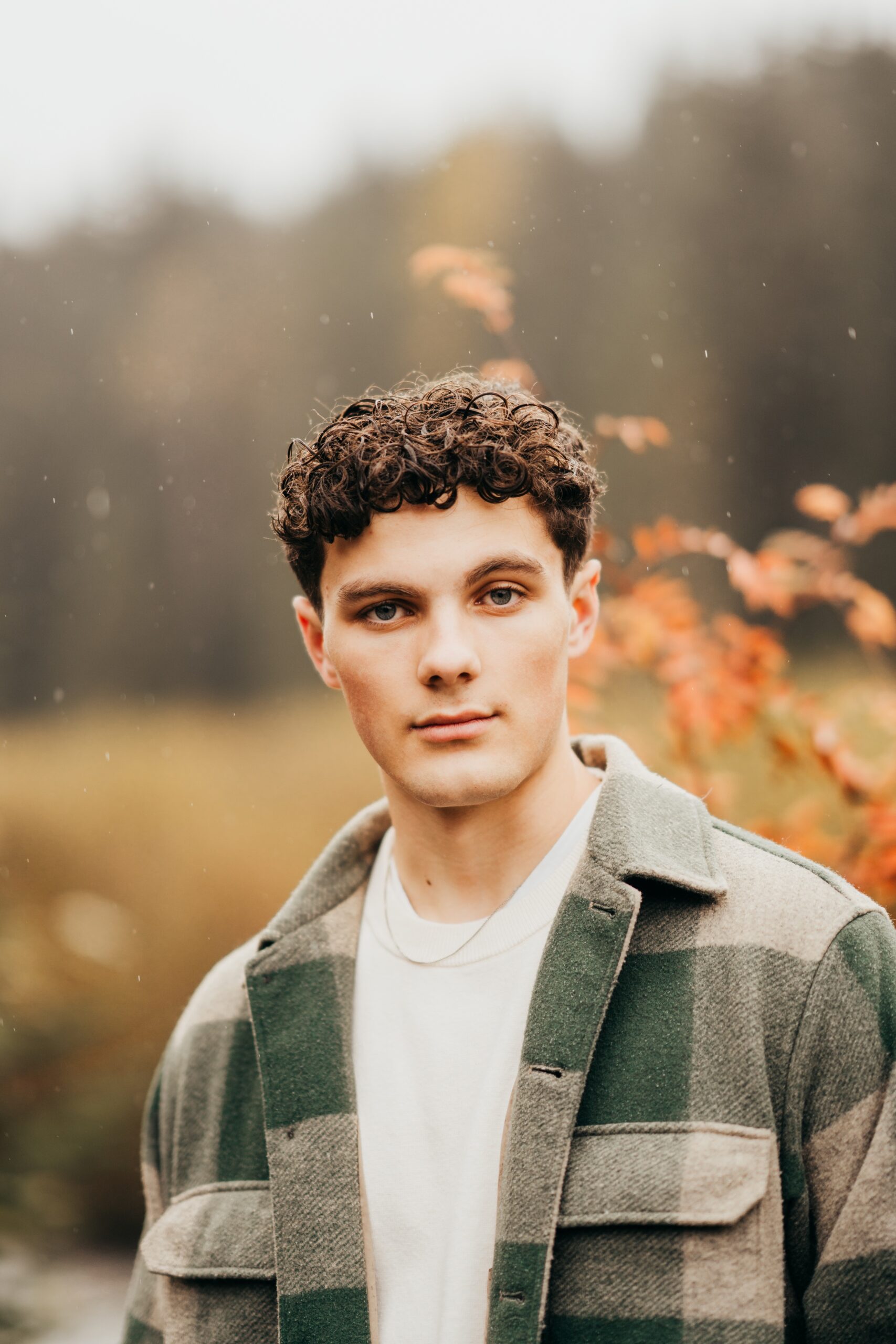 A high school senior in green plaid shirt stands in a park at sunset after visiting event venues in seattle