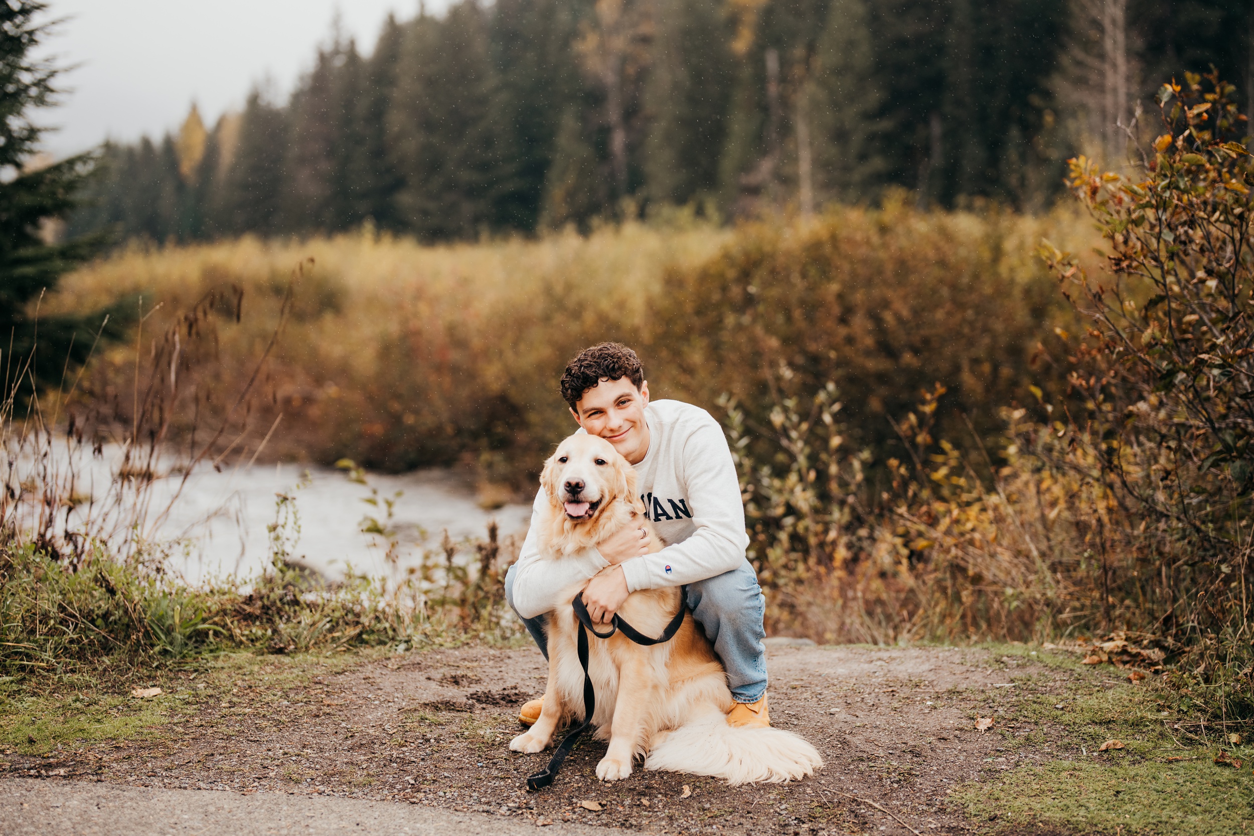A happy teenage boy hugs his golden retriever in a trail at sunset after exploring event venues in seattle
