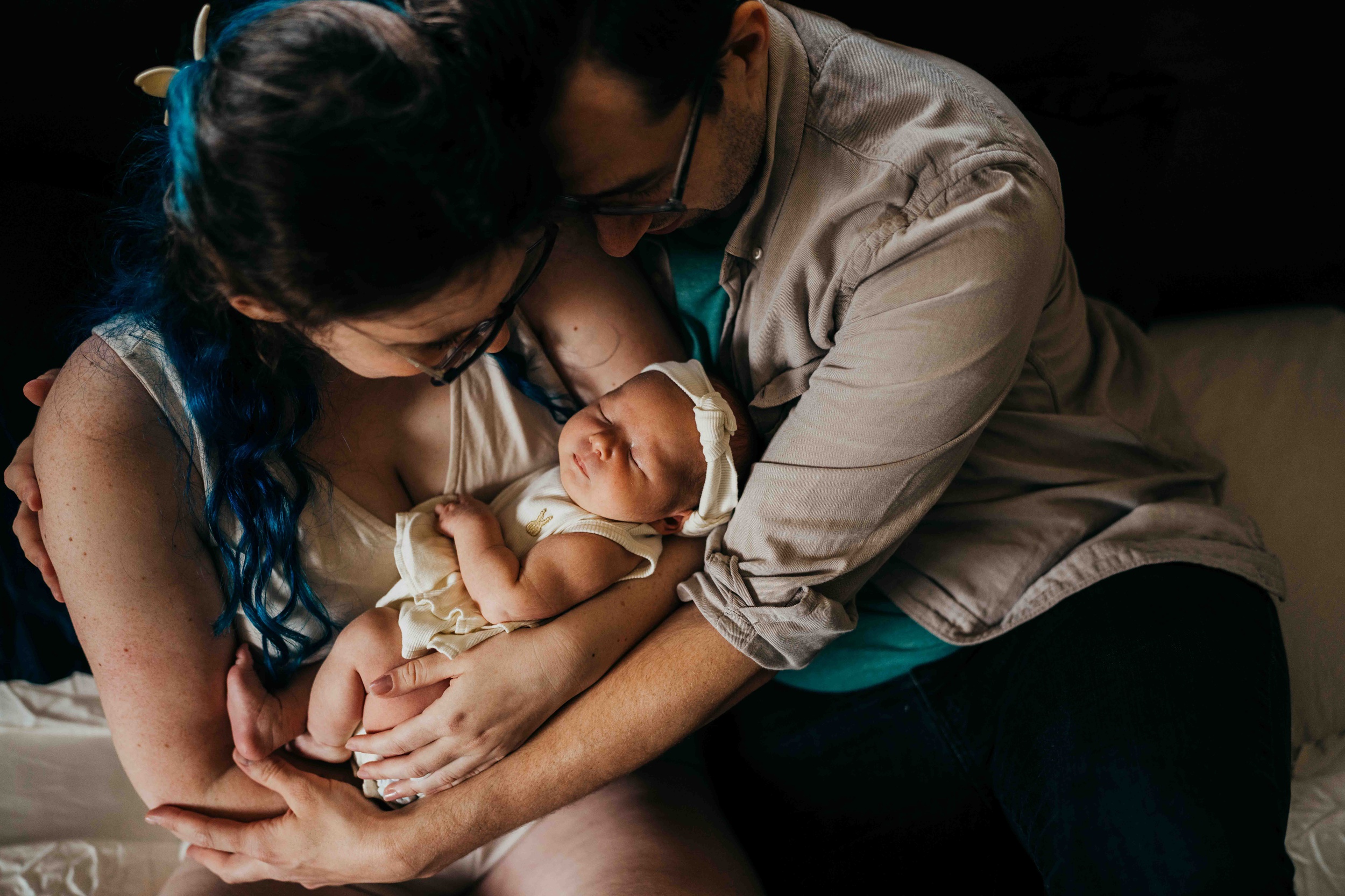 Happy new parents smile down at their sleeping newborn in mom's arms while snuggling after finding infant daycare in seattle