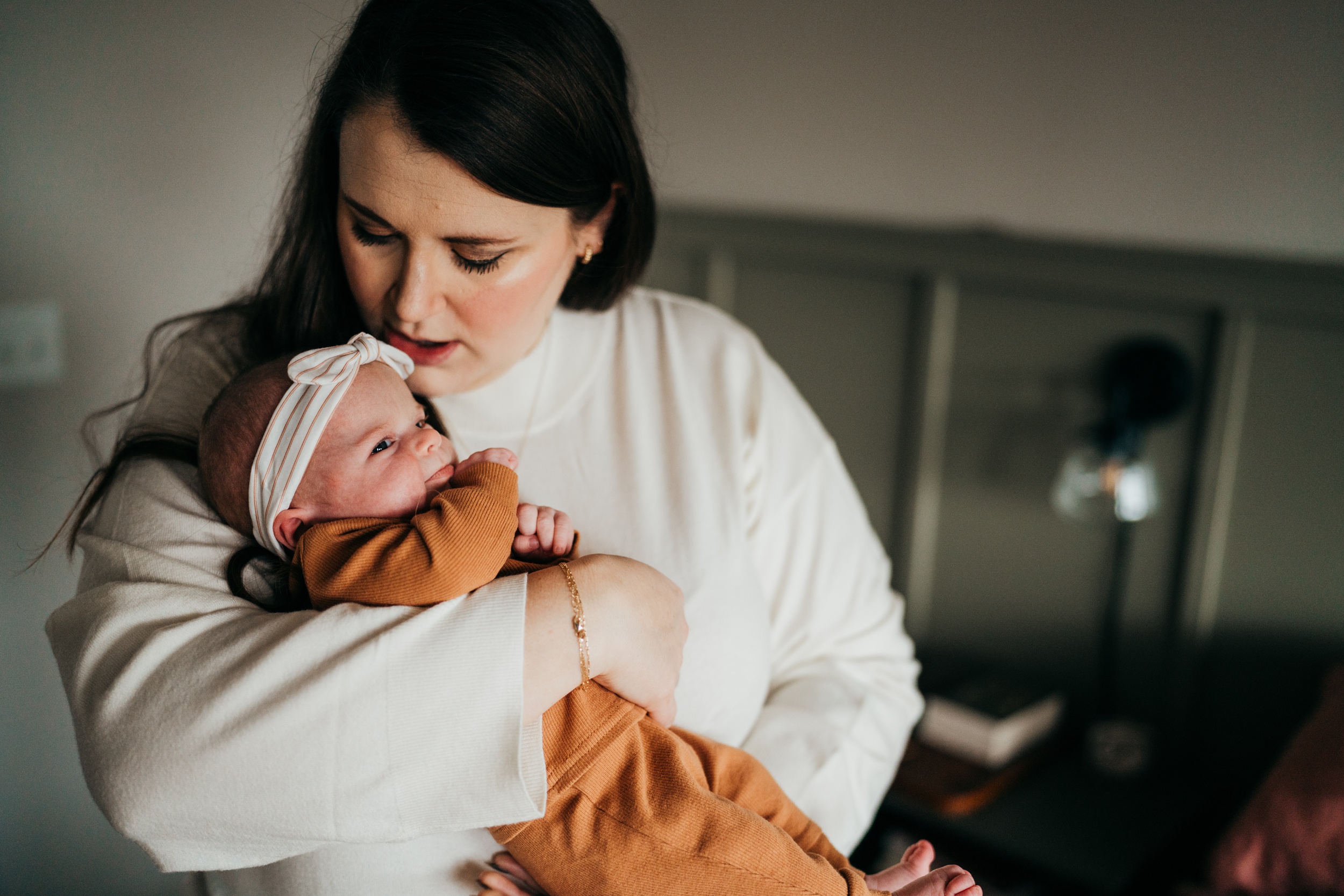 A newborn baby is kissed by mom while being held in a window in an orange onesie