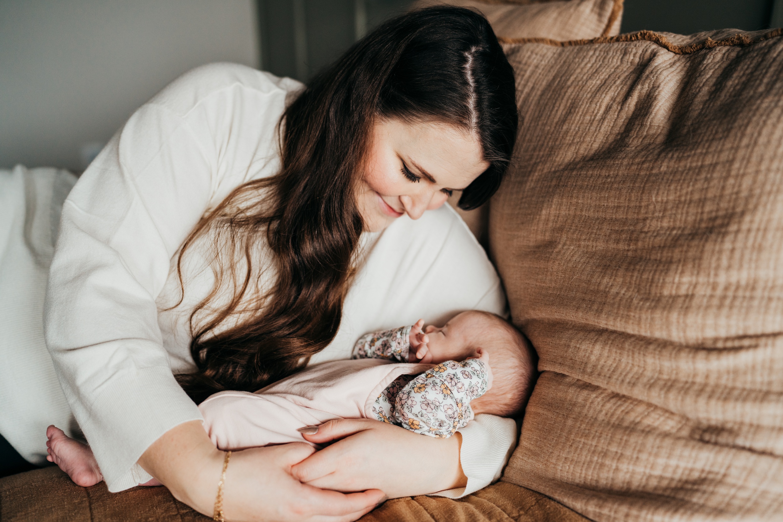 A smiling new mother lays on a bed snuggling her sleeping newborn baby after meeting lactation consultants in seattle