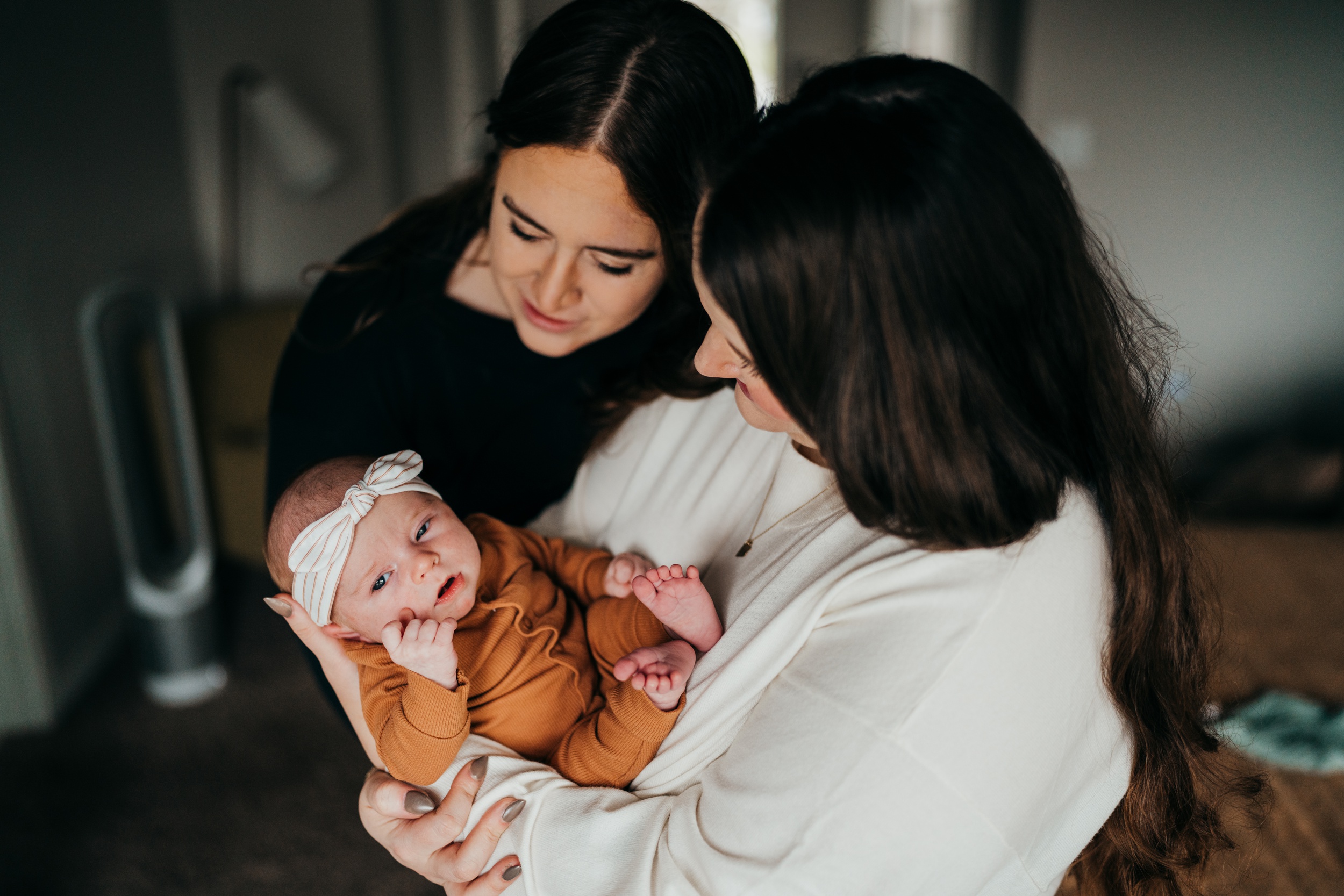 Happy new moms cradle their newborn girl in their arms in an orange onesie in a bedroom after meeting lactation consultants in seattle