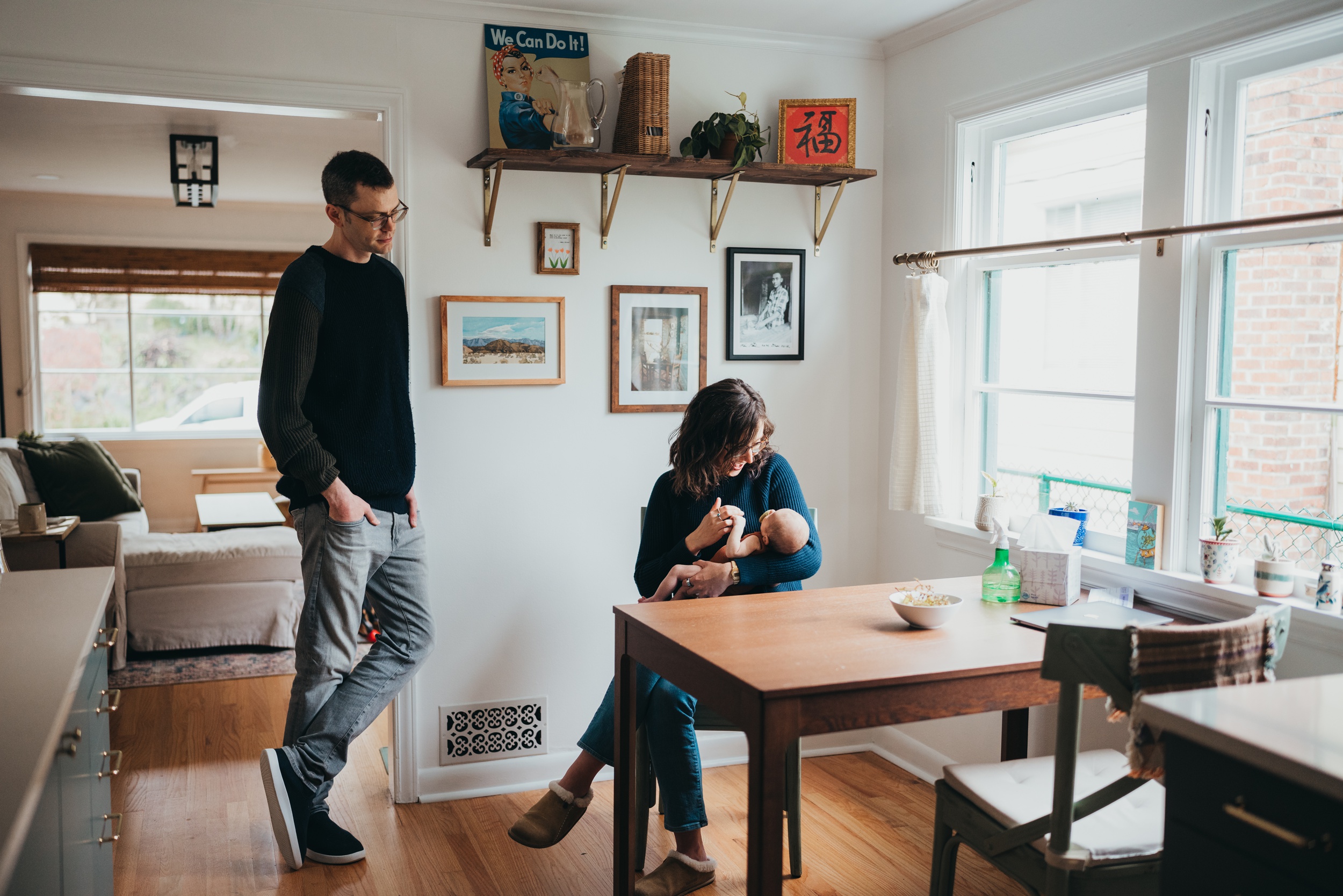 A happy mom plays with her newborn at the kitchen table as dad looks on