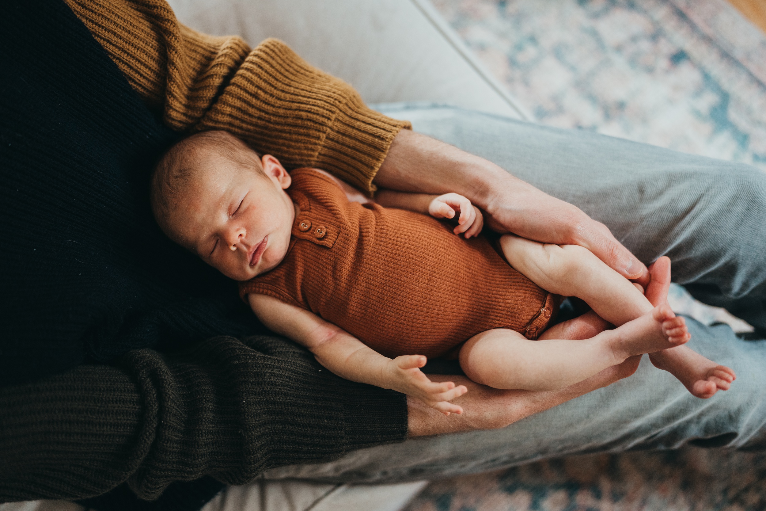 A newborn baby sleeps in dad's lap and hands in an orange onesie after meeting a mercer island nanny