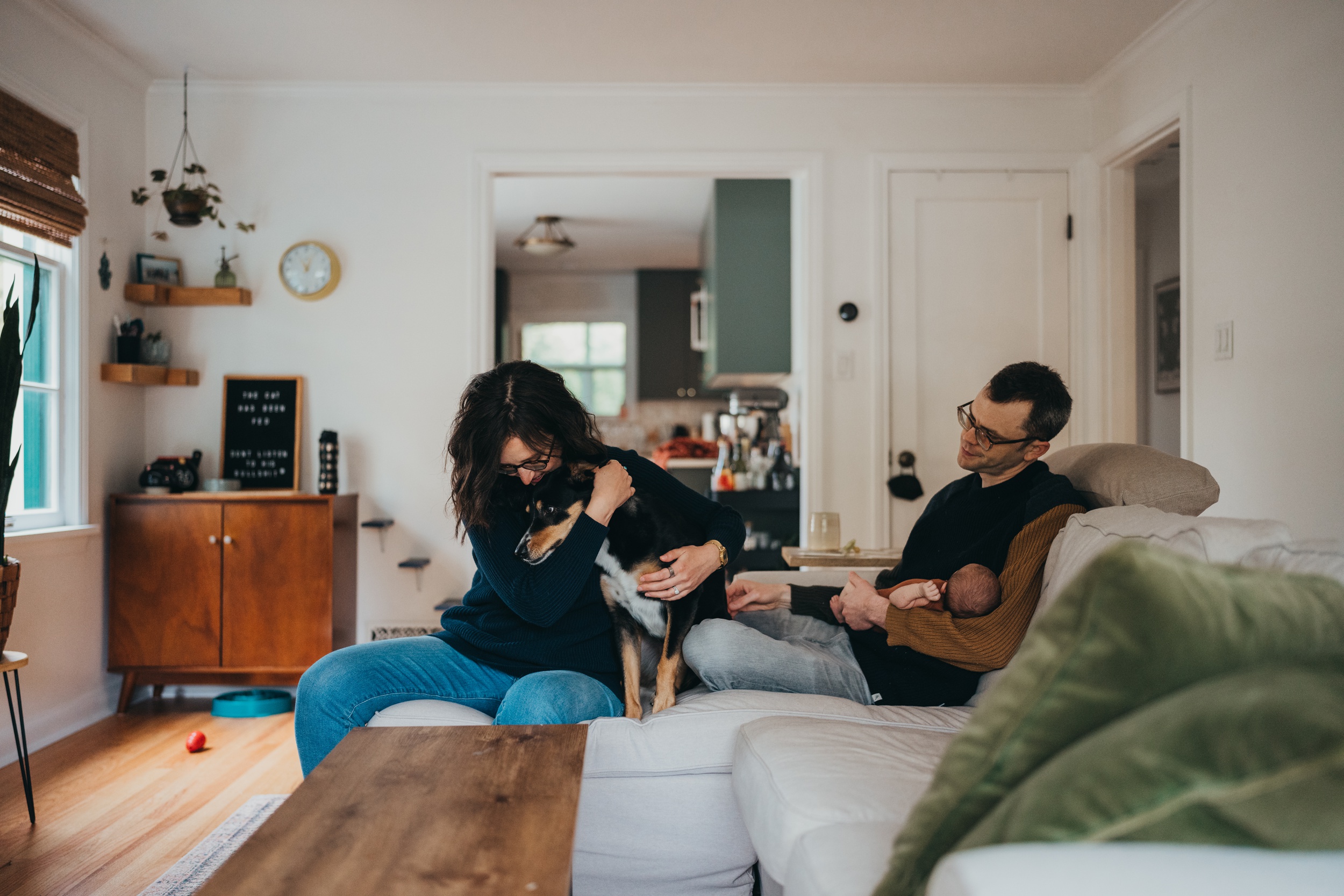 A dad cradles his newborn on a couch while mom hugs their dog after meeting a mercer island nanny