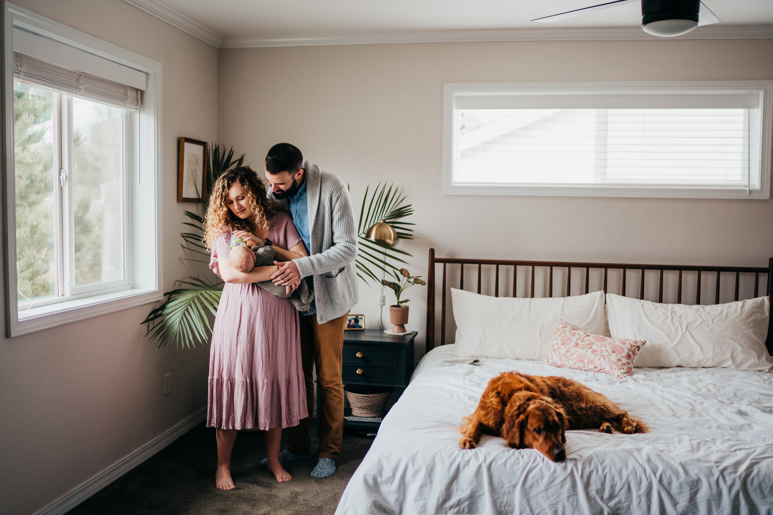 A mom and dad feed their newborn in a bedroom while their dog lays on their bed after visiting mercer island pediatrics