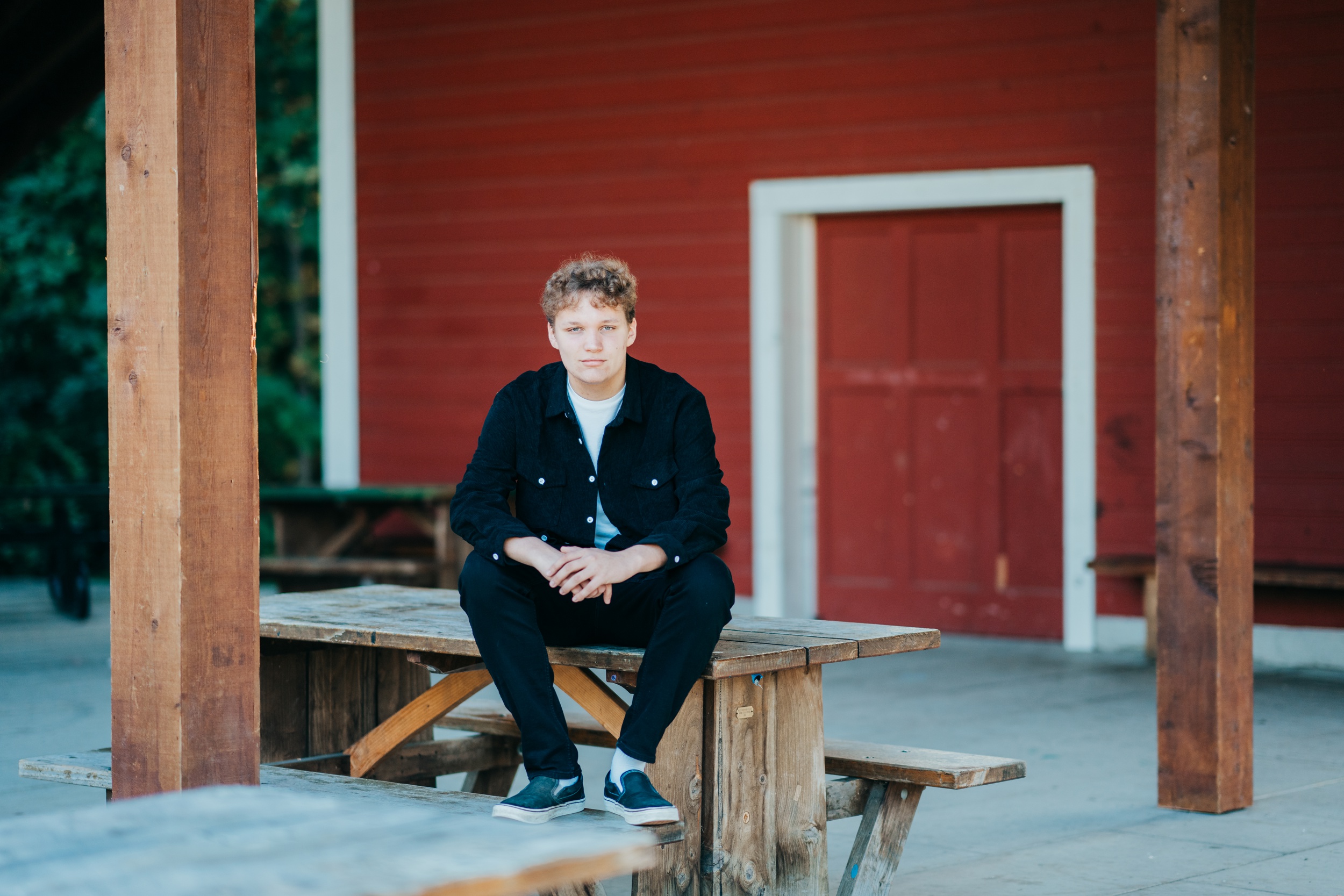 A high school grad sits on a wooden picnic table in black after enjoying mercer island tutoring