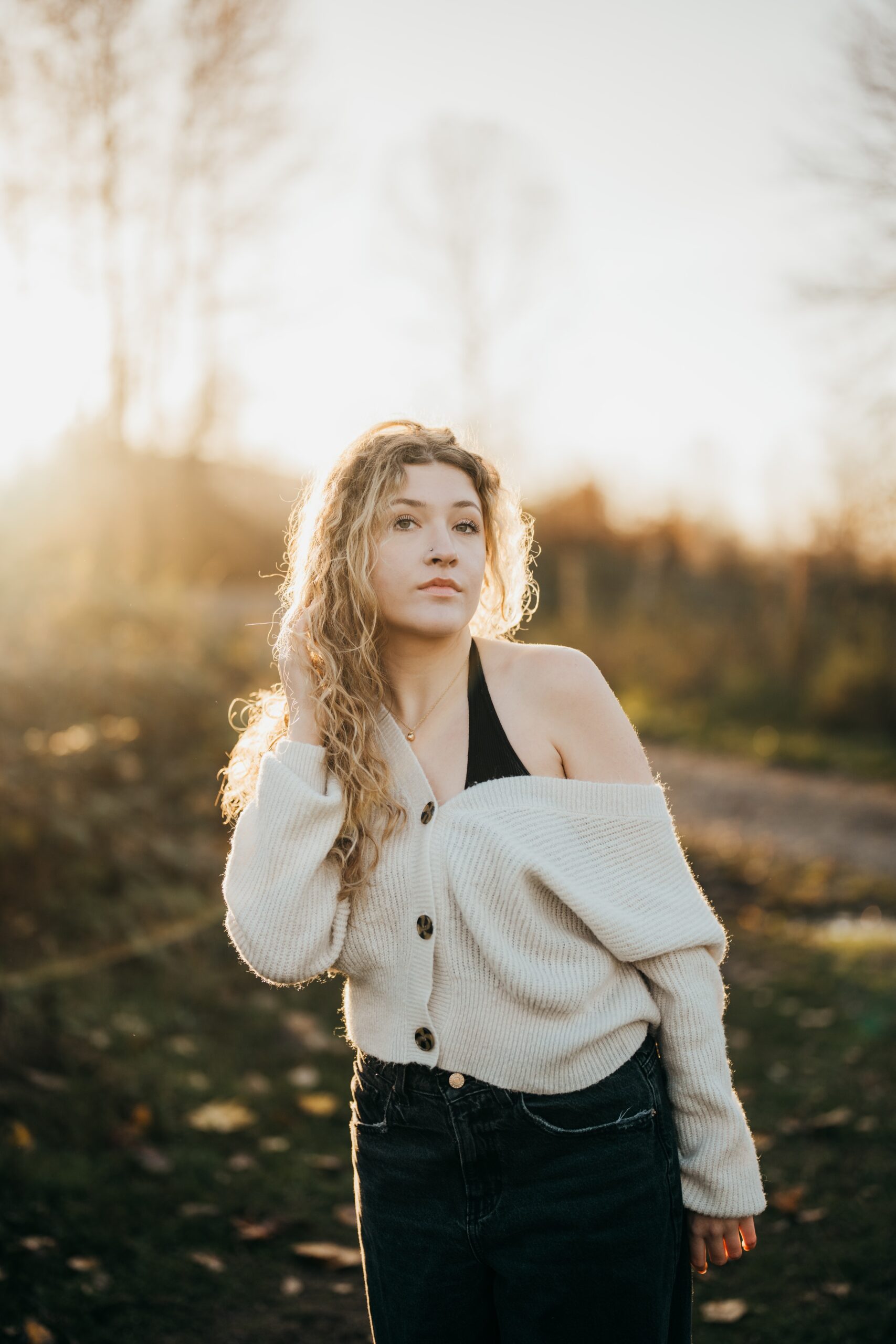 A high school senior in a white sweater off the shoulder walks in a park at sunset after visiting nail salons on mercer island