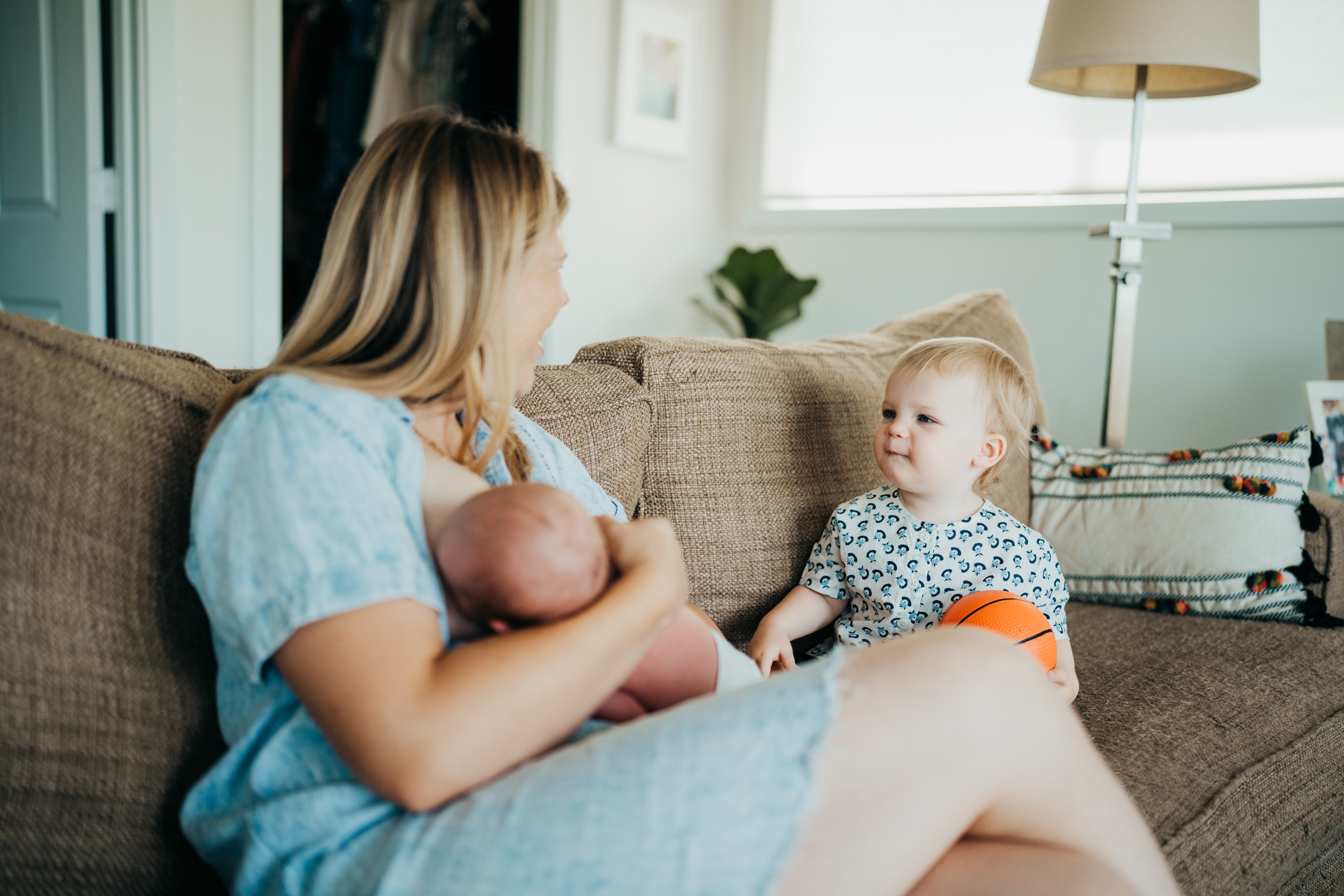 A happy mom breastfeeds on the couch while laughing with her infant son next to her