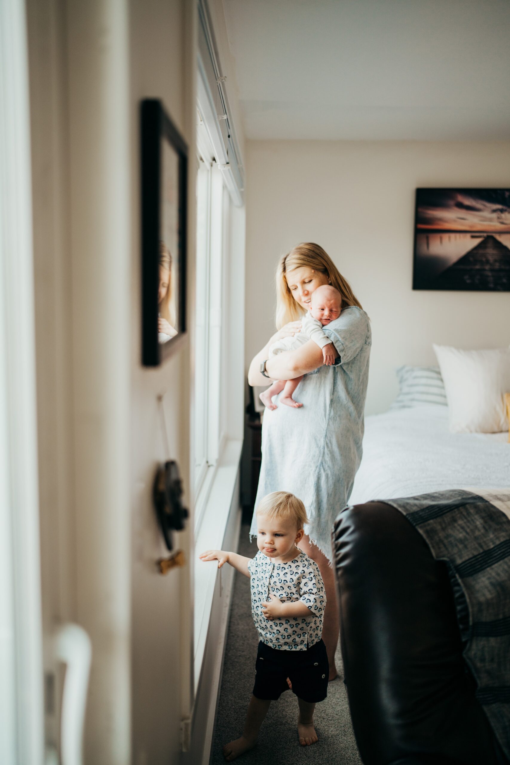 A mom cradles her newborn on her shoulder while playing with her toddler in the bedroom window after finding pediatric dentists in mercer island
