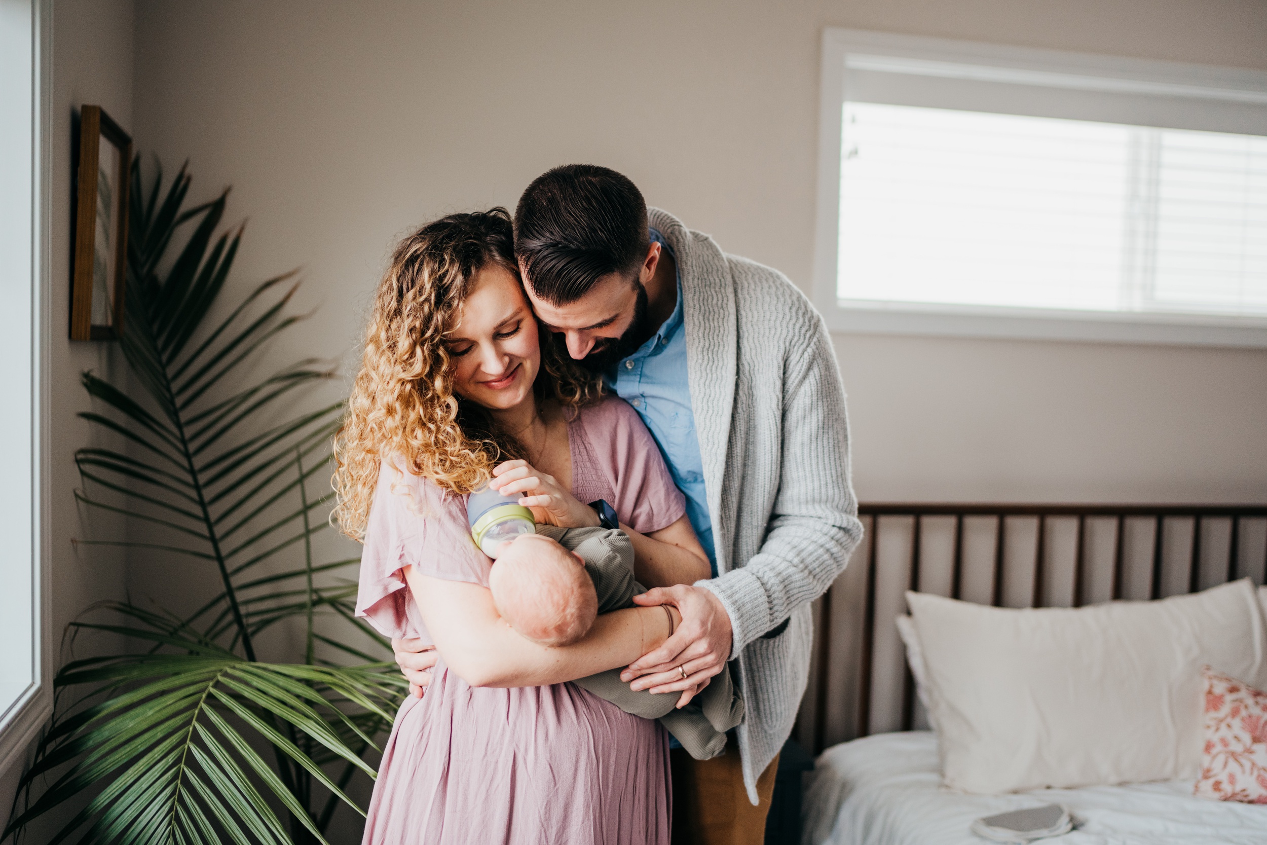 Happy new parents stand in a bedroom feeding their newborn in mom's arms after visiting pediatric dentists in seattle