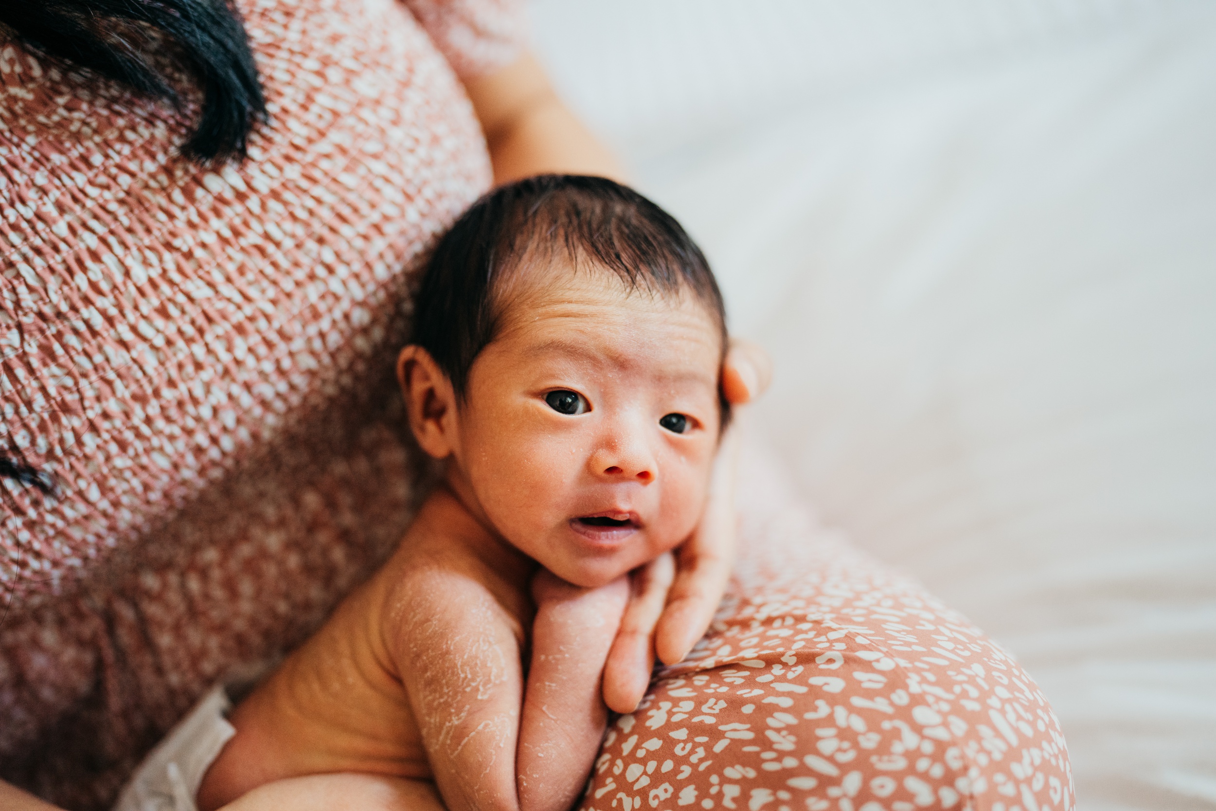 A newborn baby lays in mom's lap with eyes open