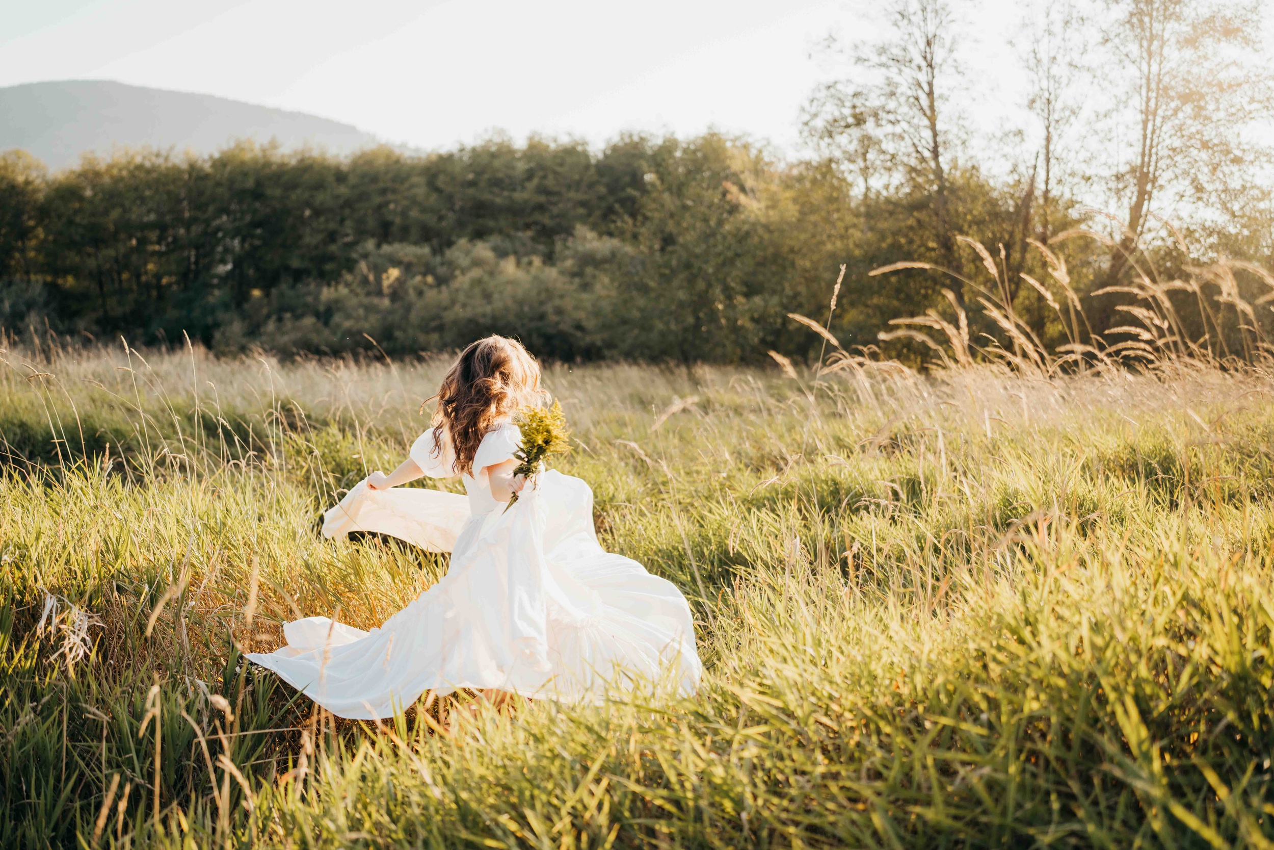 A woman in a white dress walks in a field of tall golden grass at sunset after exploring prom dress shops in seattle