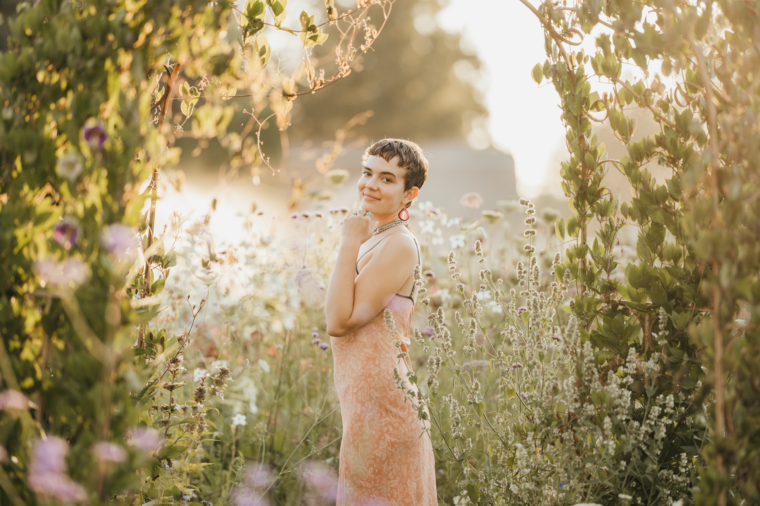 A high school senior explores a field of wildflowers at sunset in pink dress