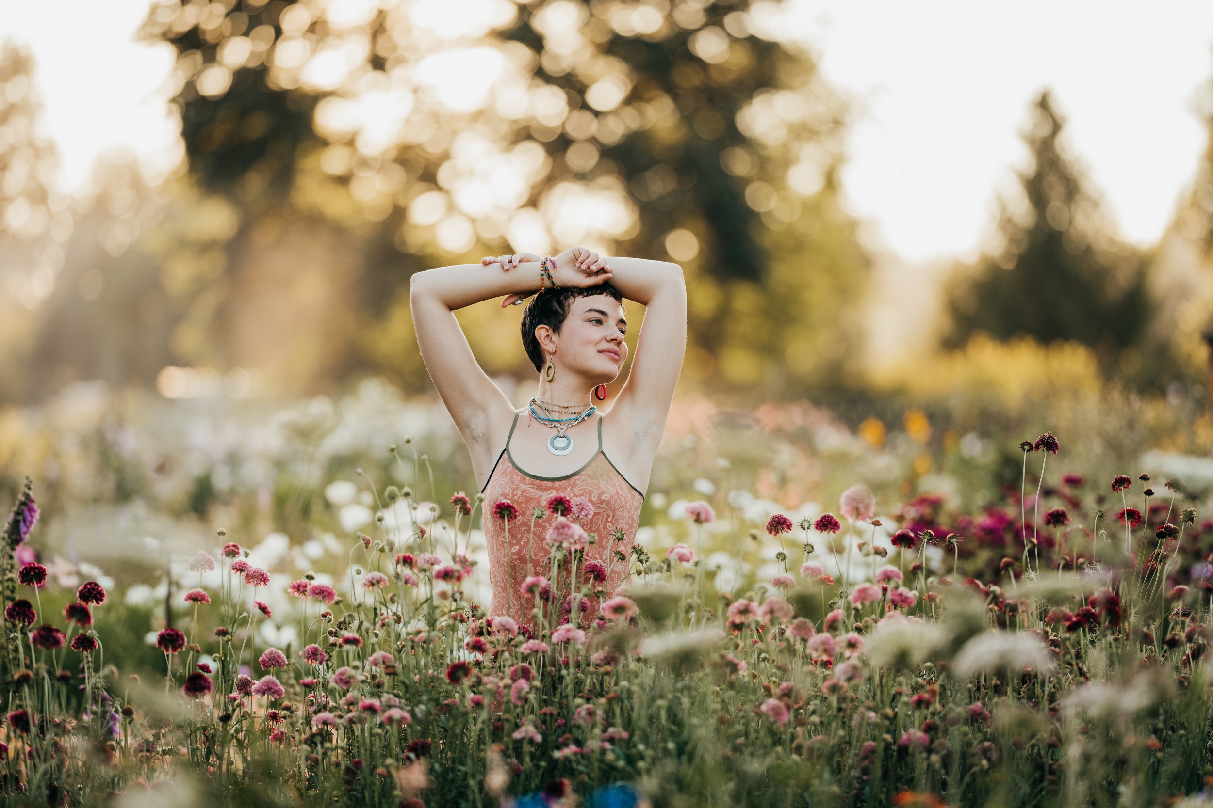 A high school grad basks in a field of wildflowers at sunset in a tank top with arms on their head after some sat prep on mercer island