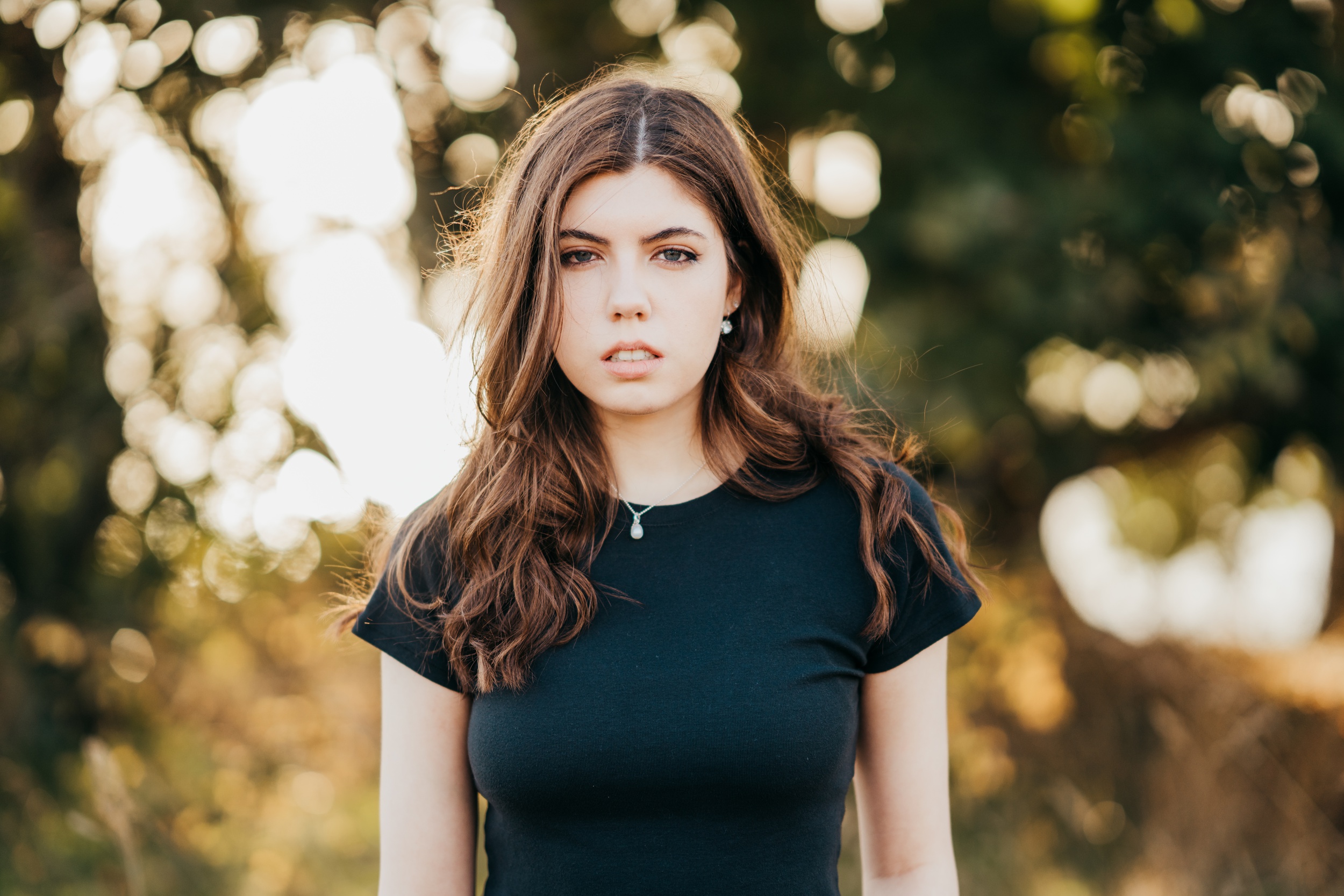 A high school senior in a black top stands in a park at sunset