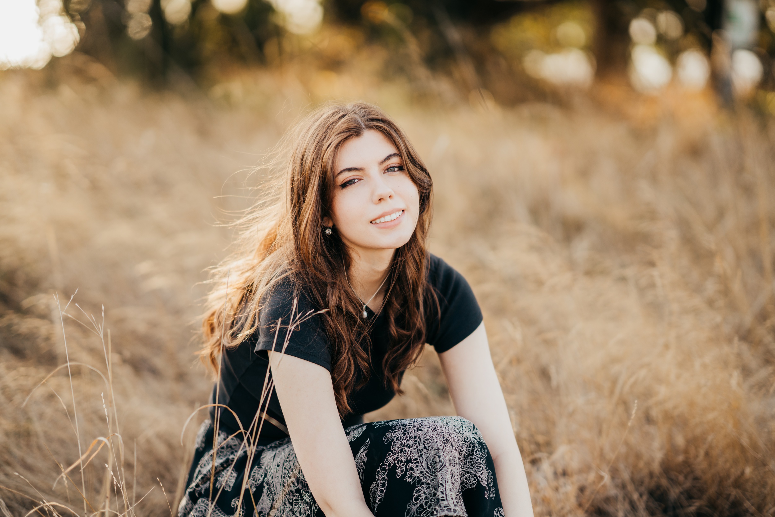 A high school senior sits in a windy field of tall golden grass in a black top smiling after finding sat prep in seattle