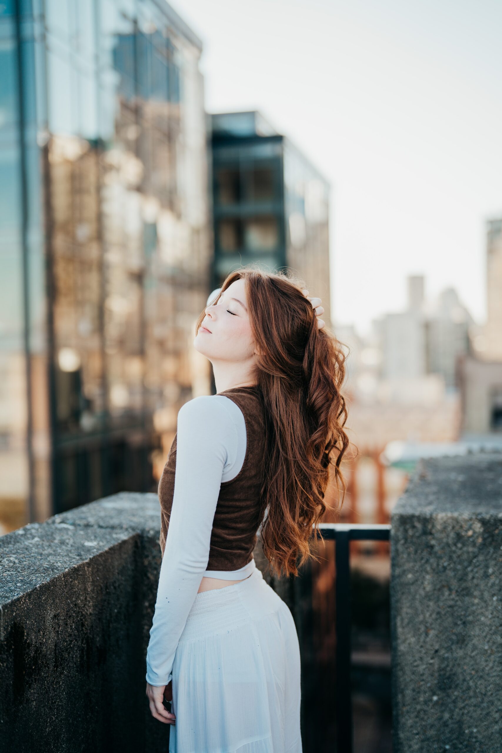 A happy high school senior in a white skirt stands on a rooftop in downtown pulling her hair back after finding tutoring in seattle