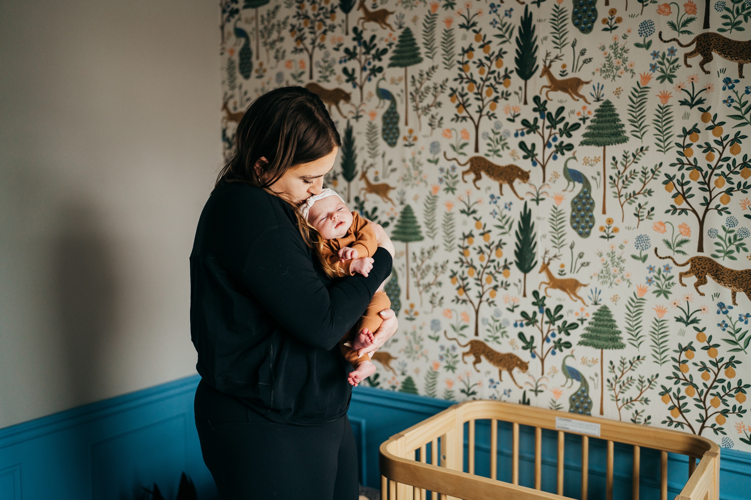 A new mom kisses her sleeping newborn in her arms while standing in a nursery after some baby music classes in seattle
