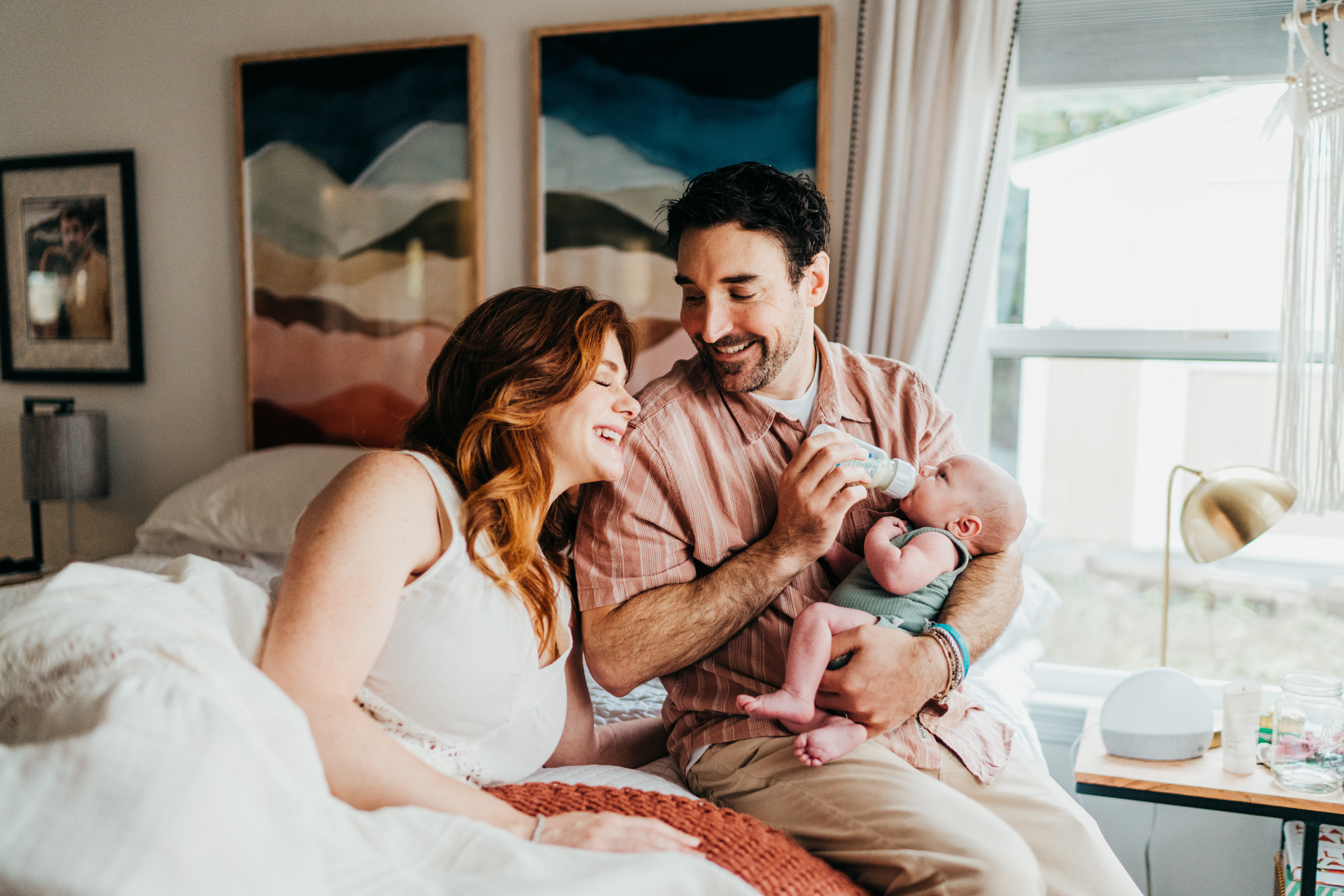 Laughing new parents bottle feed their newborn in bed