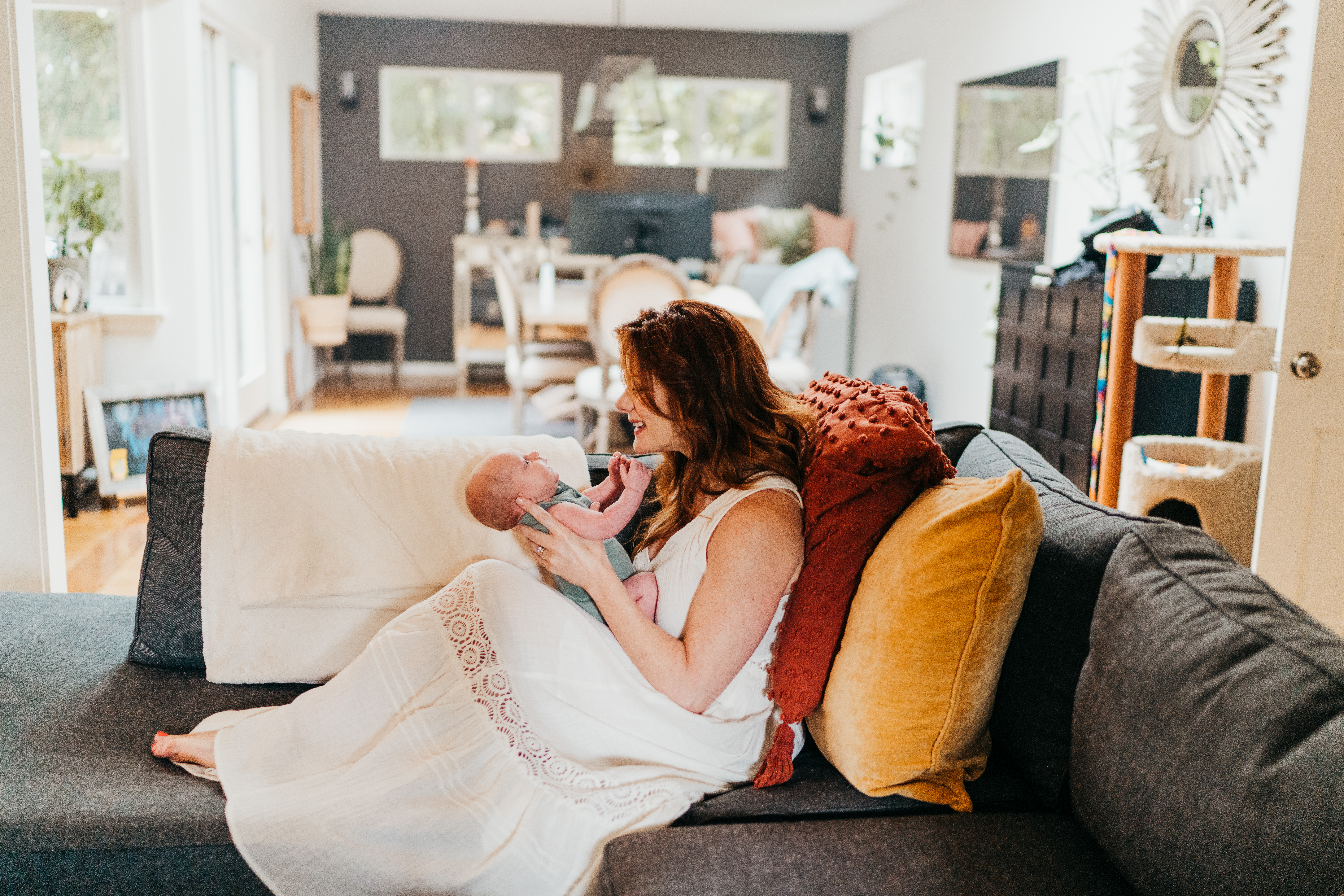 A happy new mom sits across a couch playing with her newborn in her lap after finding baby proofing in seattle