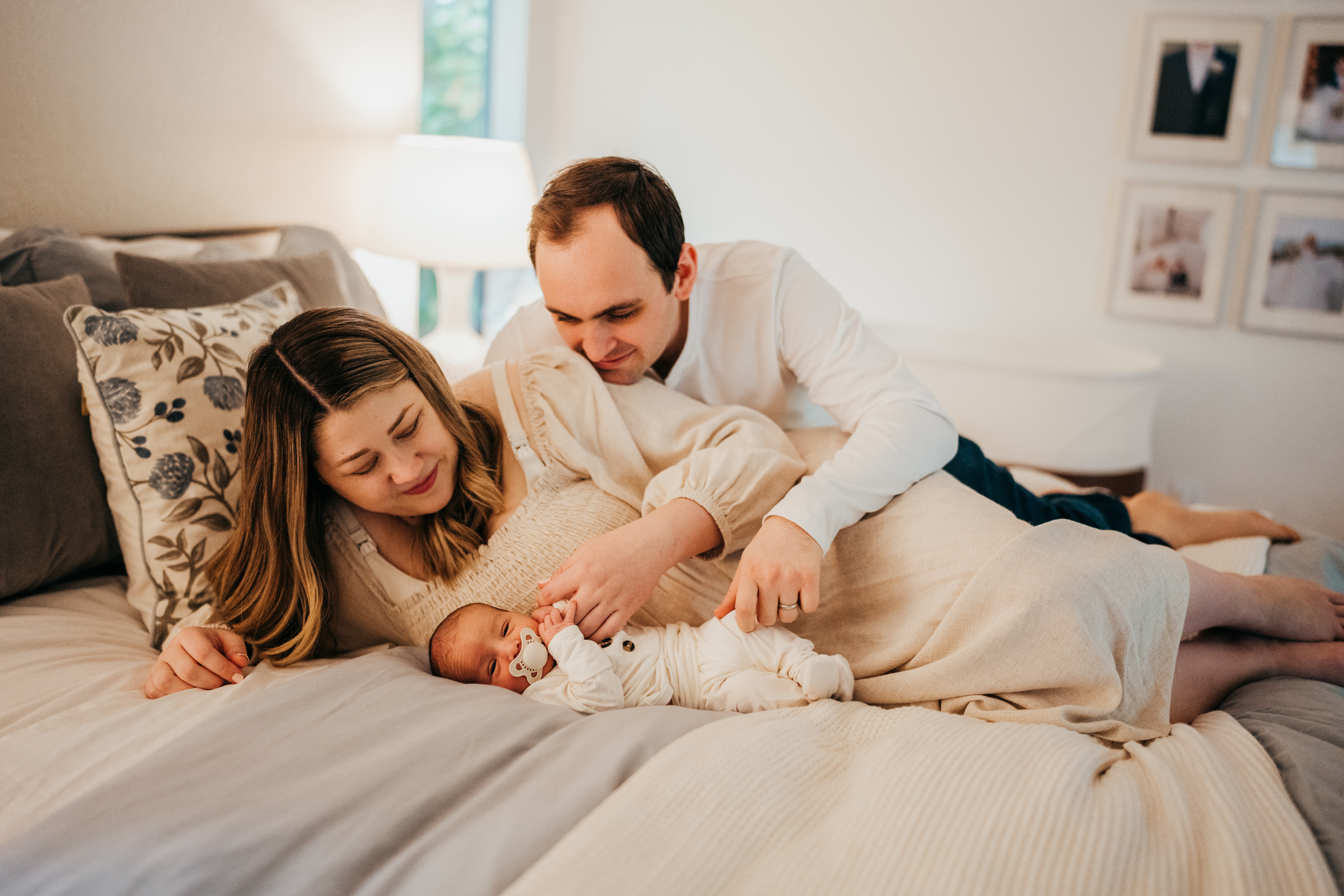 Happy new parents snuggle on a bed with their newborn