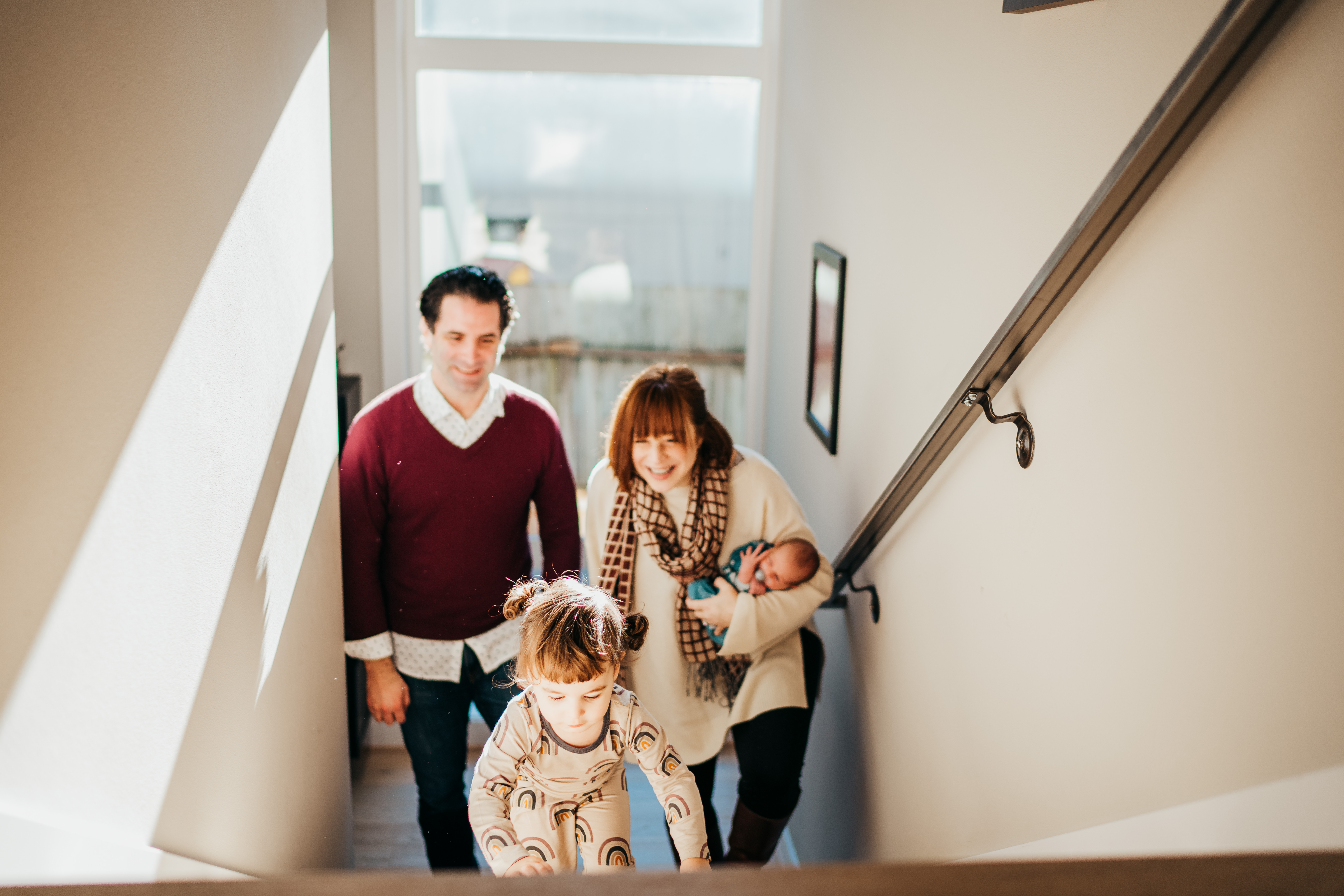 A toddler girl climbs the stairs in front of mom and dad in rainbow pajamas before visiting baby story time in seattle
