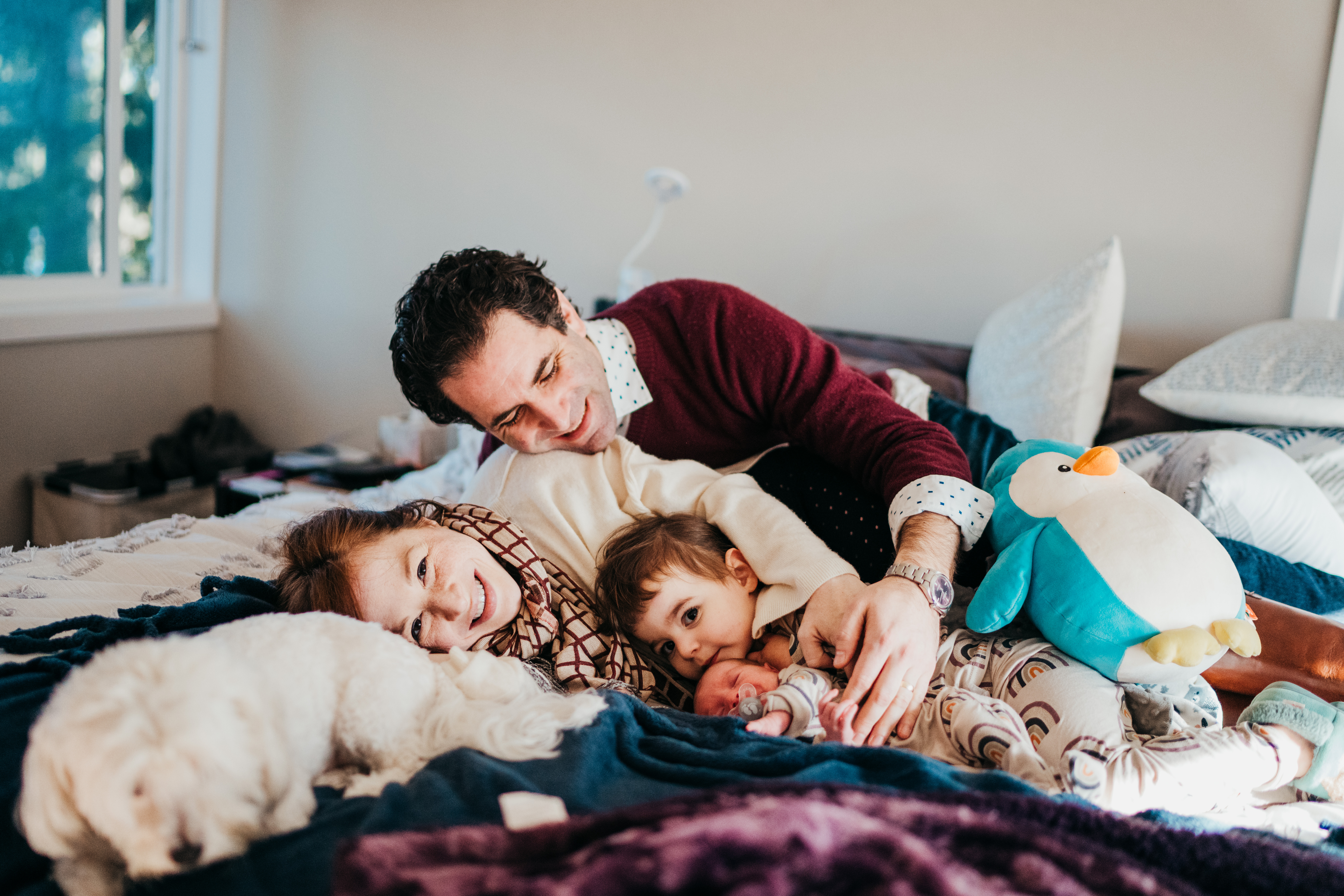 Mom and dad snuggle their newborn and toddler in matching pajamas on a bed before visiting baby story time in seattle