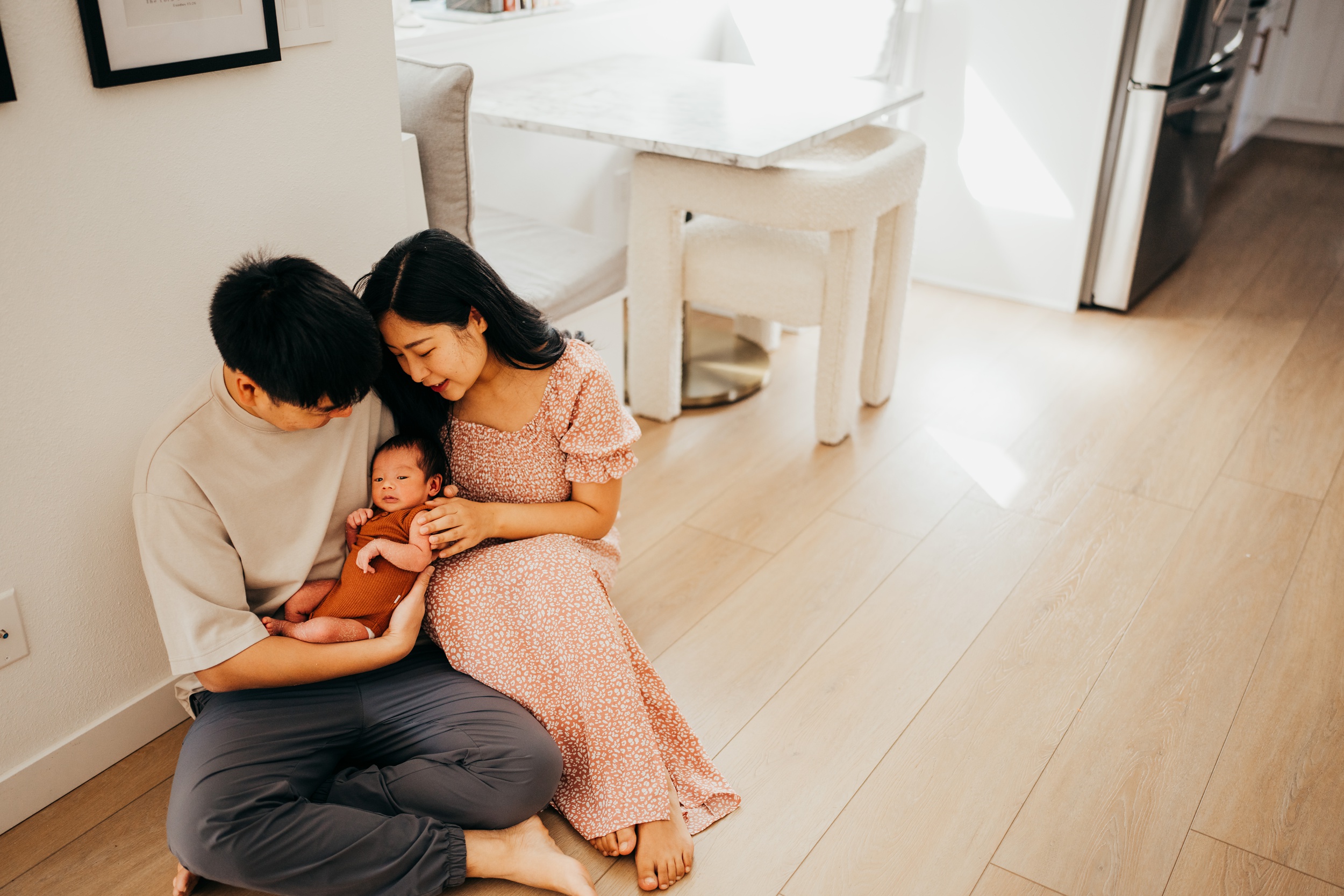 Happy new parents sit on the kitchen floor snuggling their newborn baby