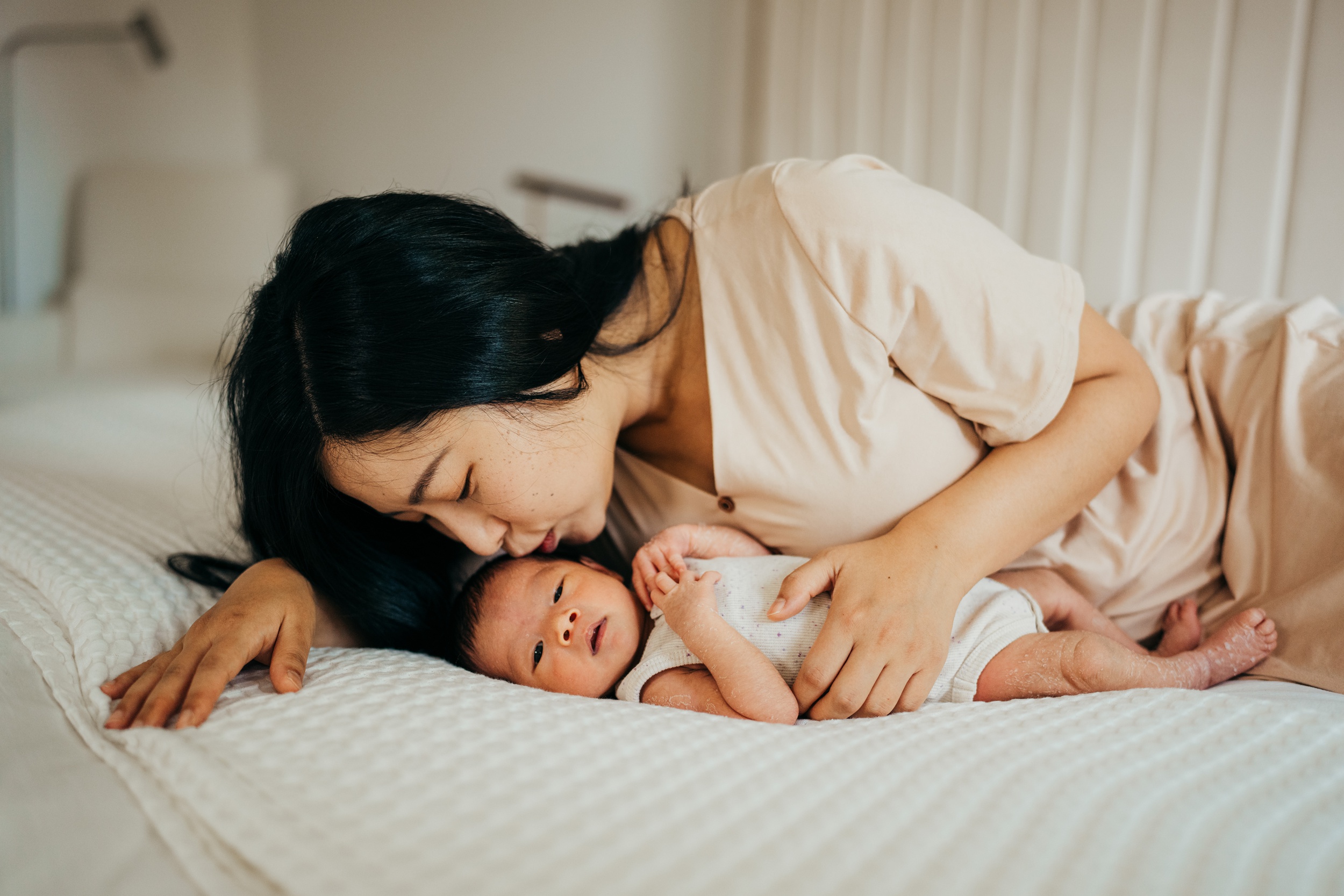 A new mom snuggles and kisses her newborn baby on a bed after meeting emerald city doulas