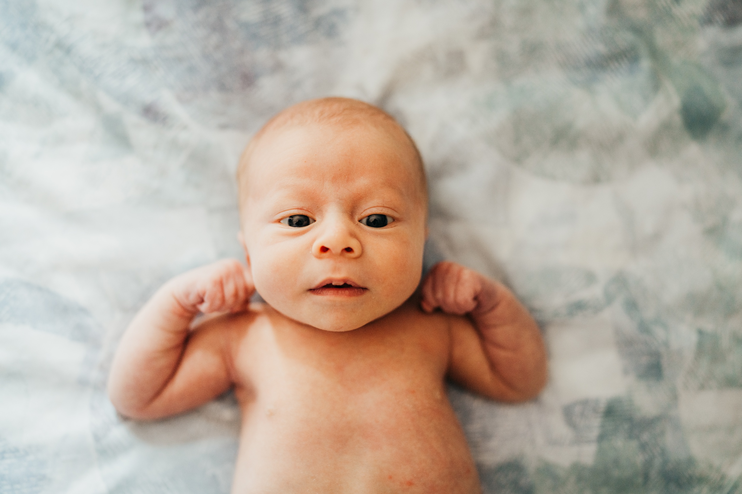 A newborn baby lays on a bed with arms flexing after an infant massage in seattle
