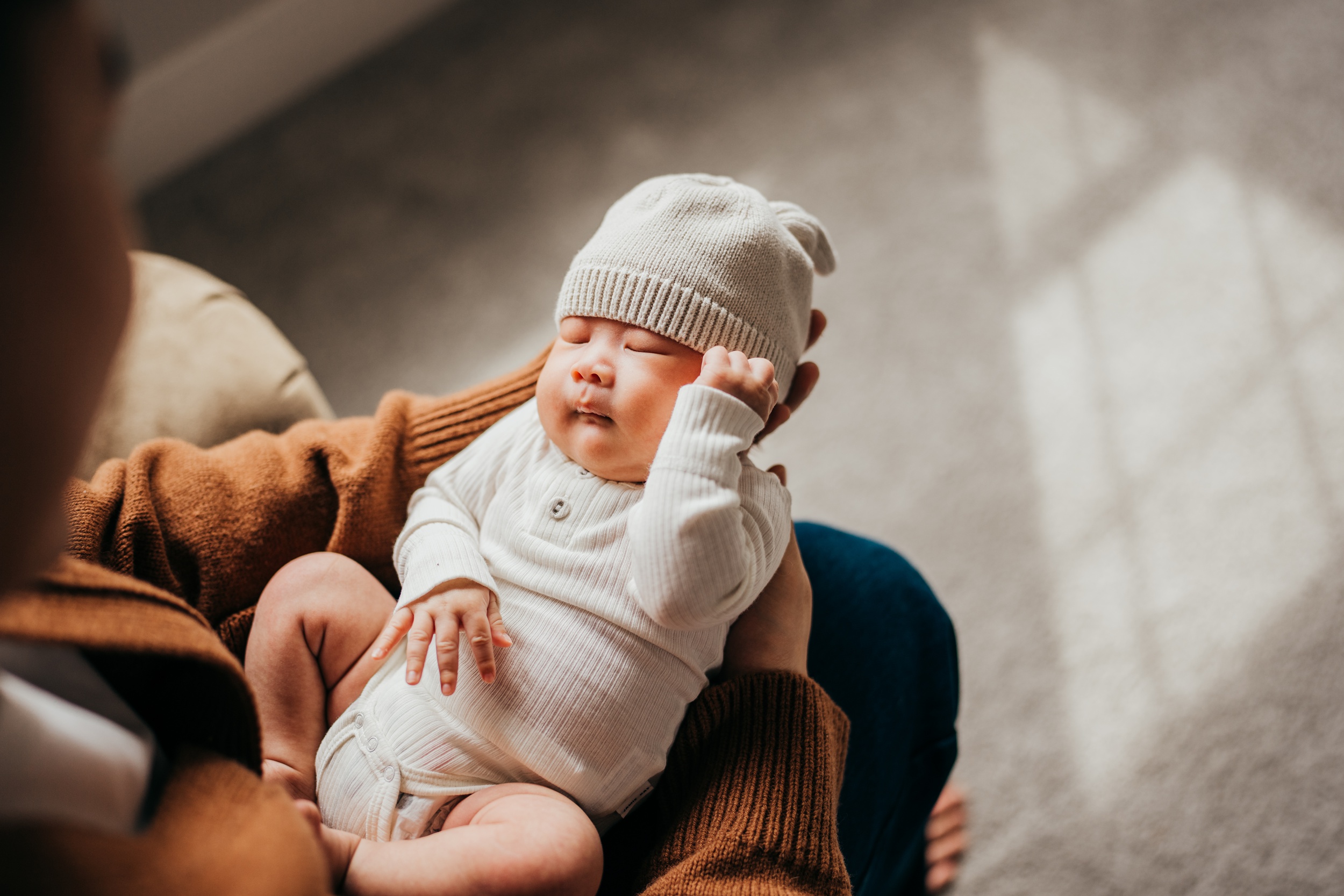 A newborn baby in a white onesie and sleep cap sleeps in dad's hands and laps thanks to maternal fetal medicine in seattle