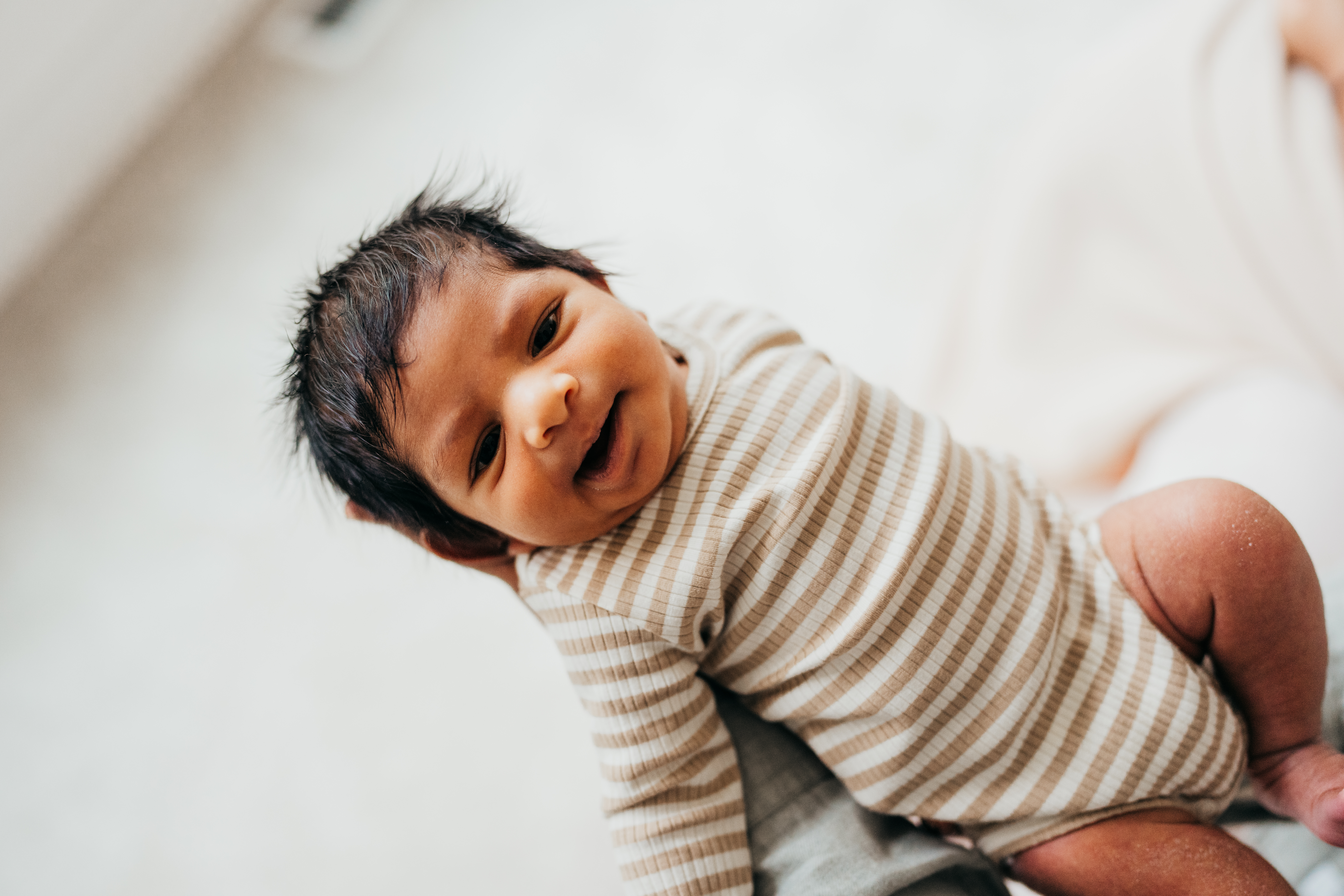 A happy baby lays in dad's hand in a stripe onesie